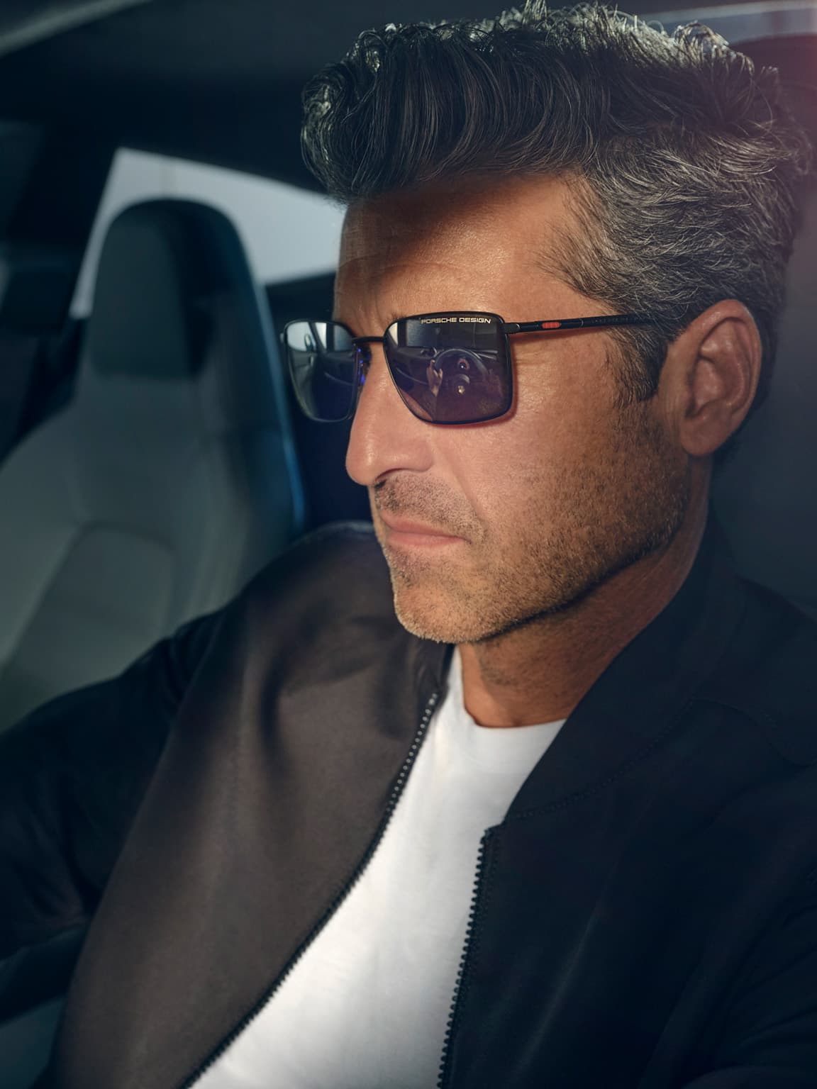 Patrick Dempsey sitting in a Porsche wearing Porsche Design sunglasses