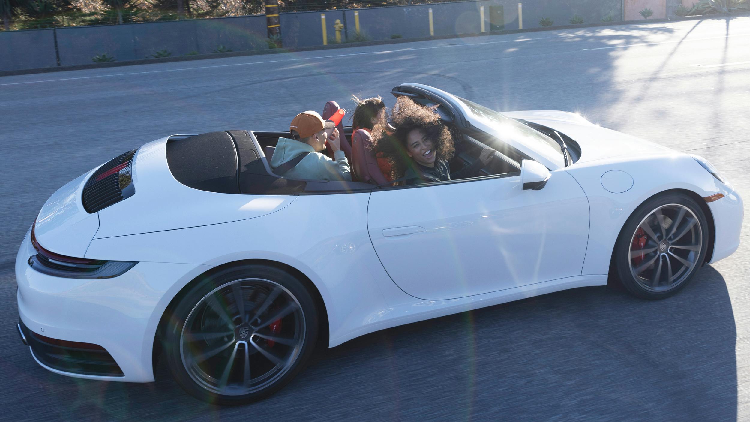 Three people riding in a convertible white Porsche 911