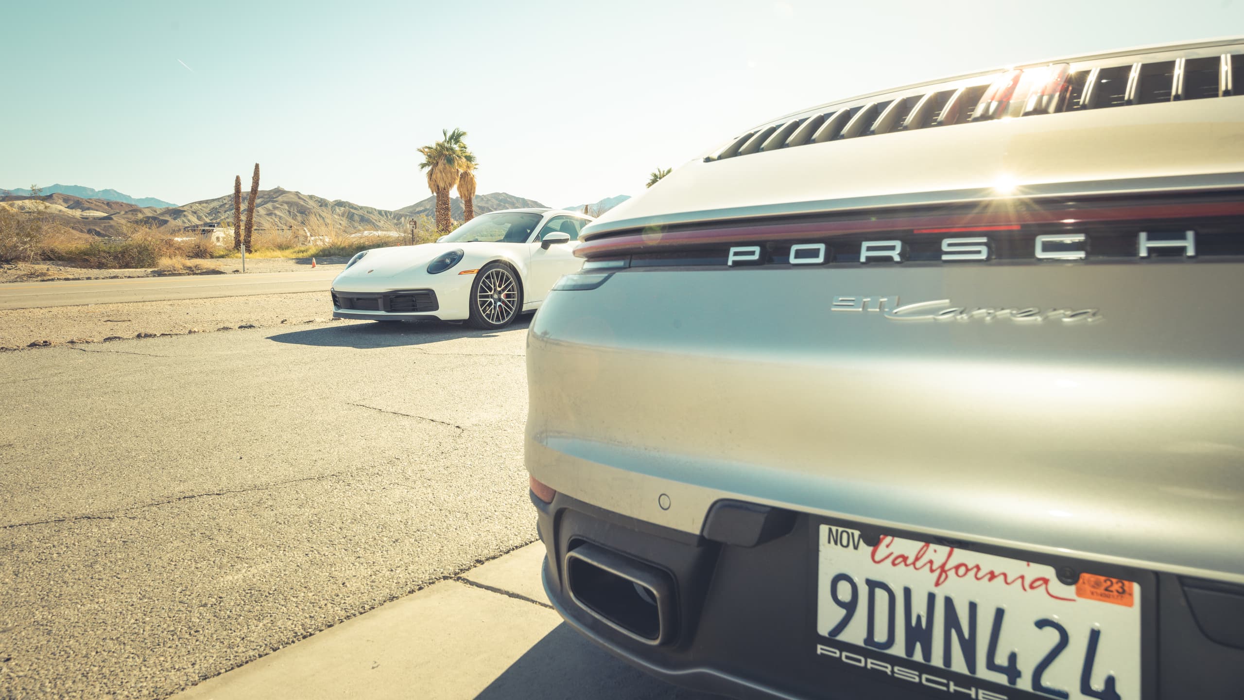 Shown is a cutout of a silver Porsche 911 from behind and on the opposite street a white Porsche 911 from the front.