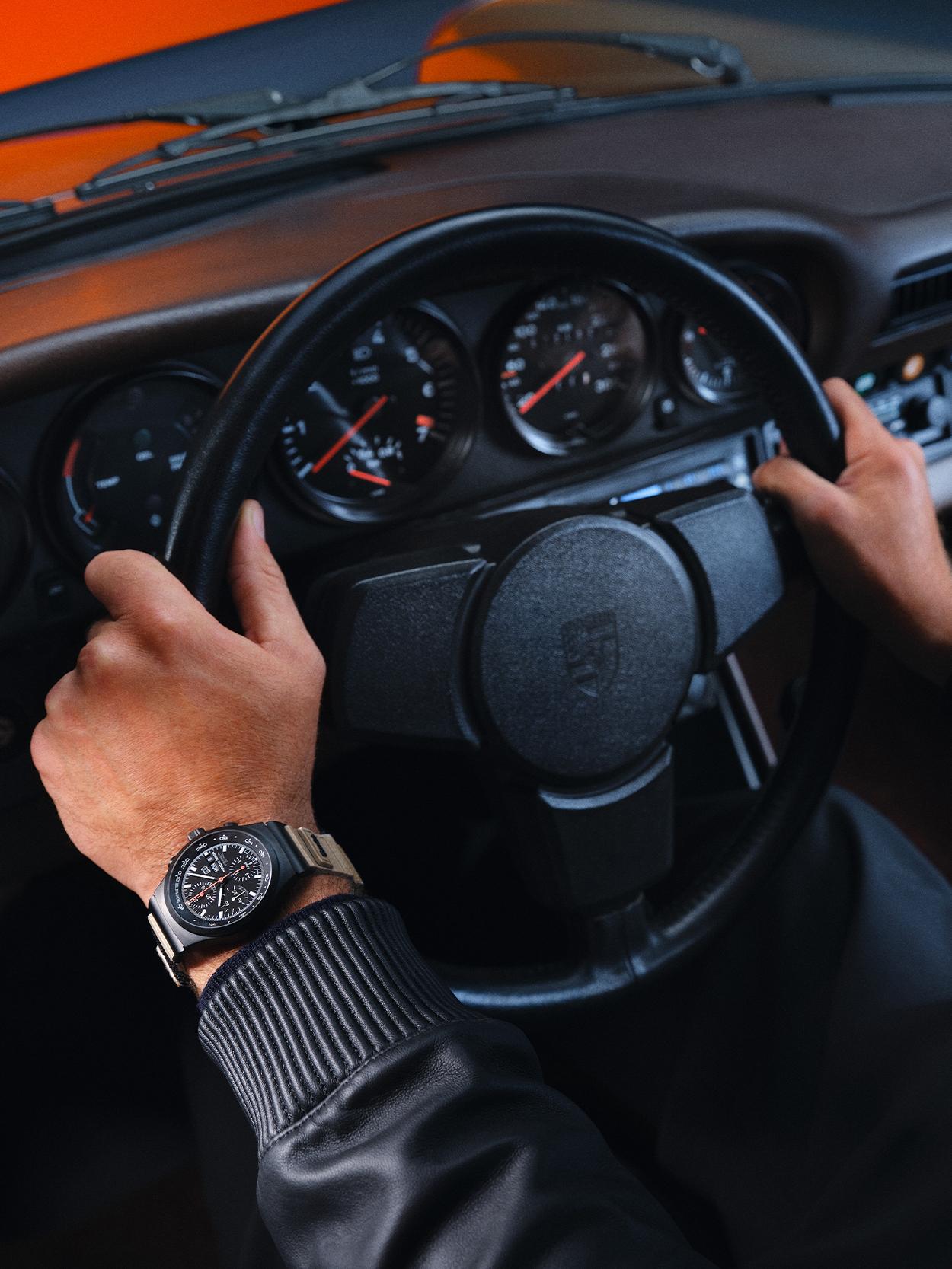 Person is sitting behind a steering wheel in a historic Porsche car and is wearing new Porsche 50Y Chronograph