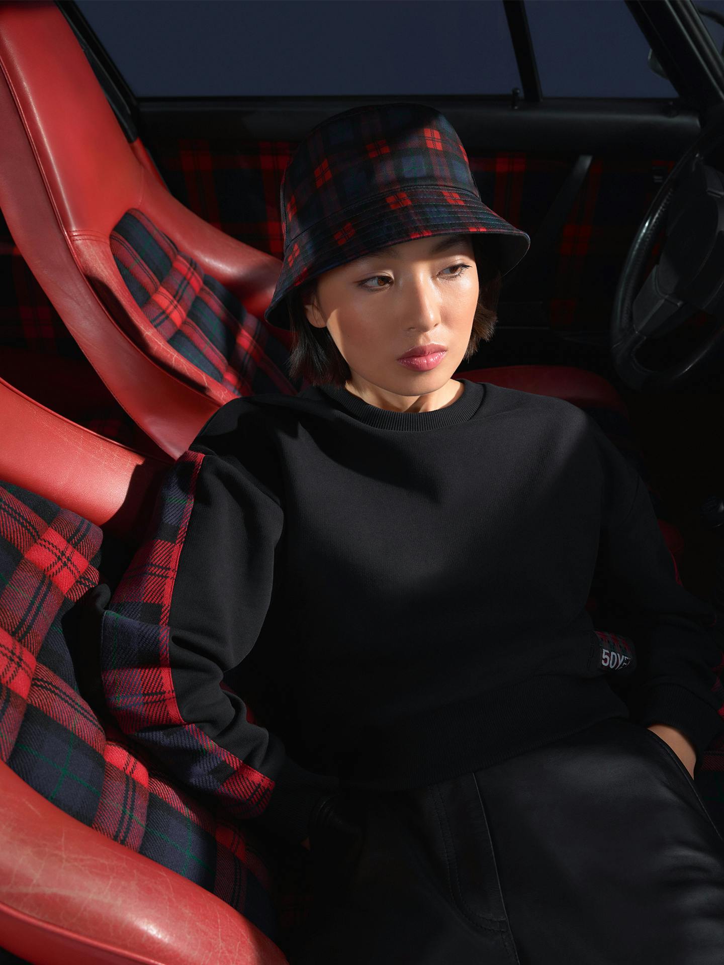 Woman is sitting in the car and wearing clothing from the Porsche Turbo No. 1 Collection