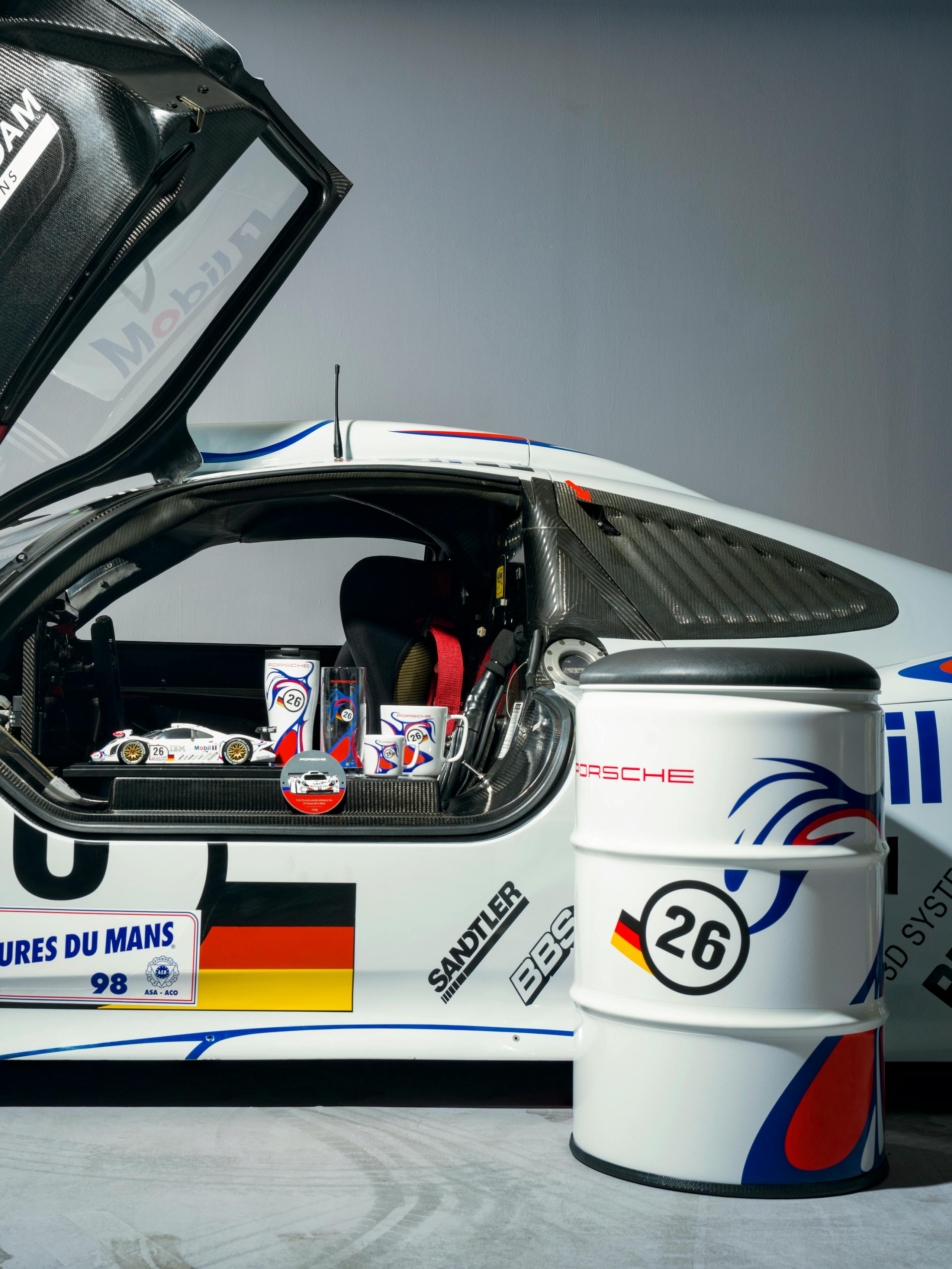 You can see a white Porsche with colourful details. In the foreground there is a barrel.