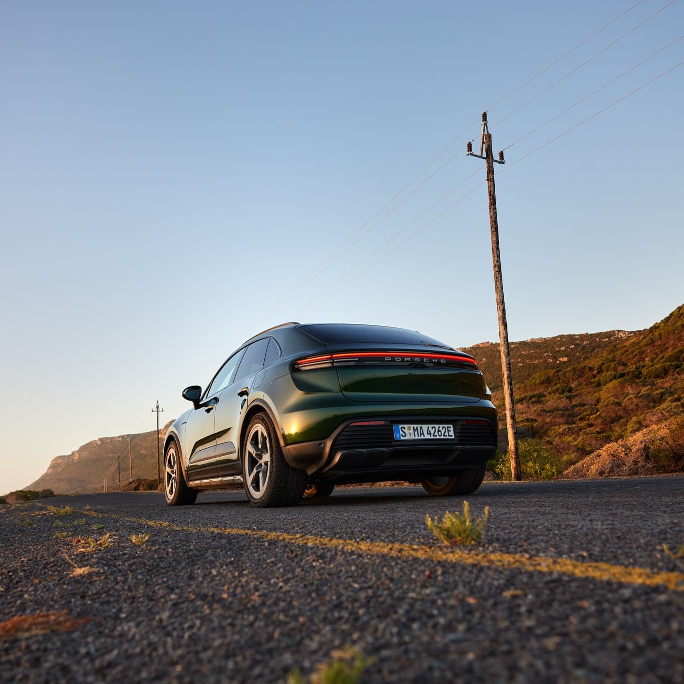 A man is standing in front of a darkgreen Porsche Macan next to a road