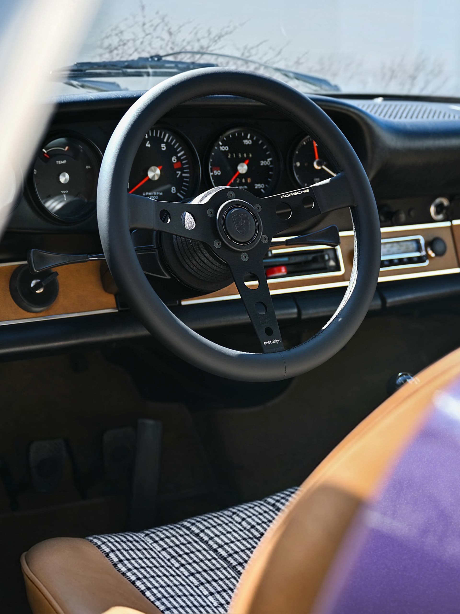 Vintage Porsche interior with black steering wheel, classic gauges, and tan leather seats, showcasing retro design elements.