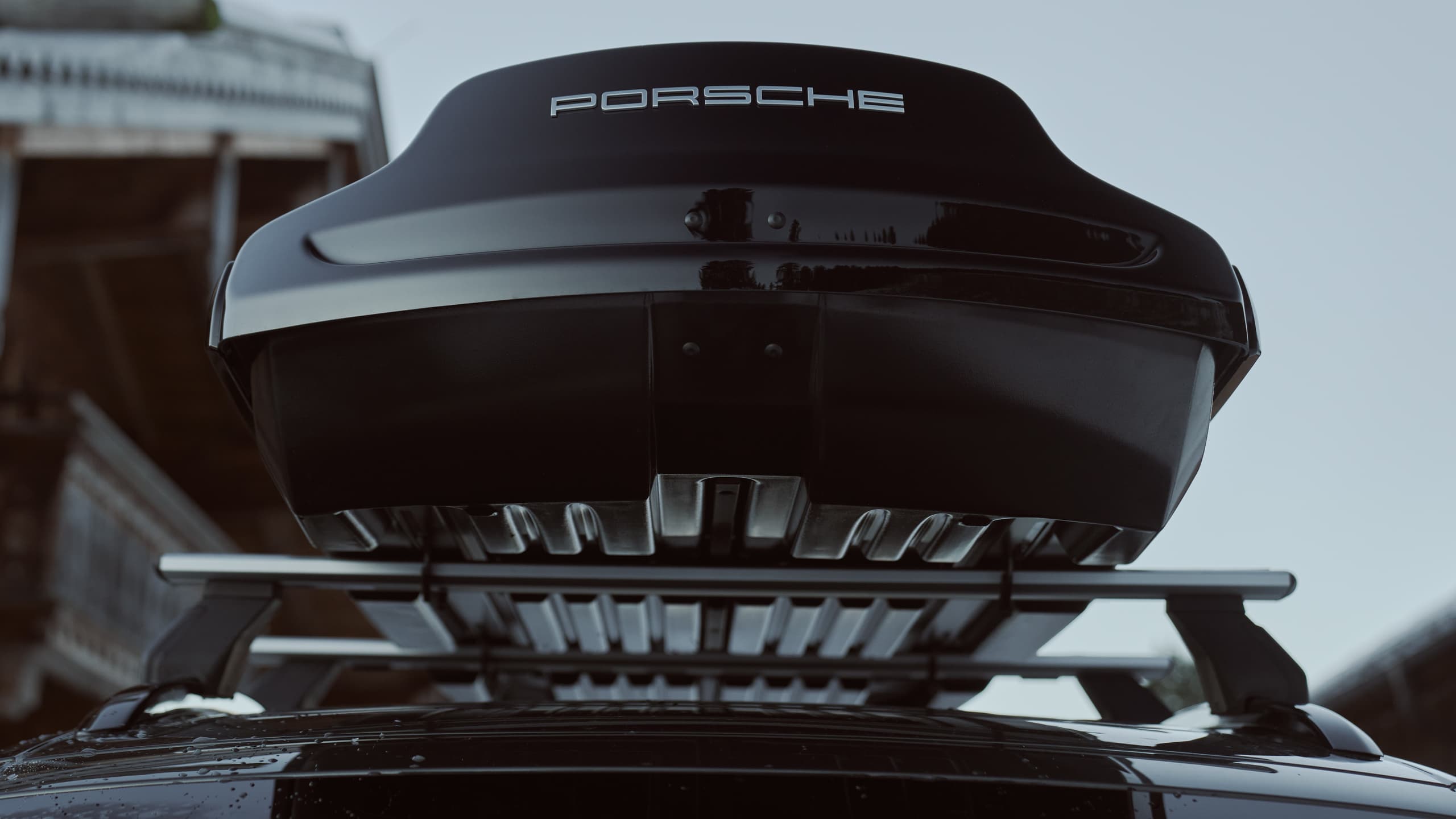 Boîte de toit noire Porsche sur voiture, vue de dessous, avec design élégant et logo visible contre un ciel dégagé.