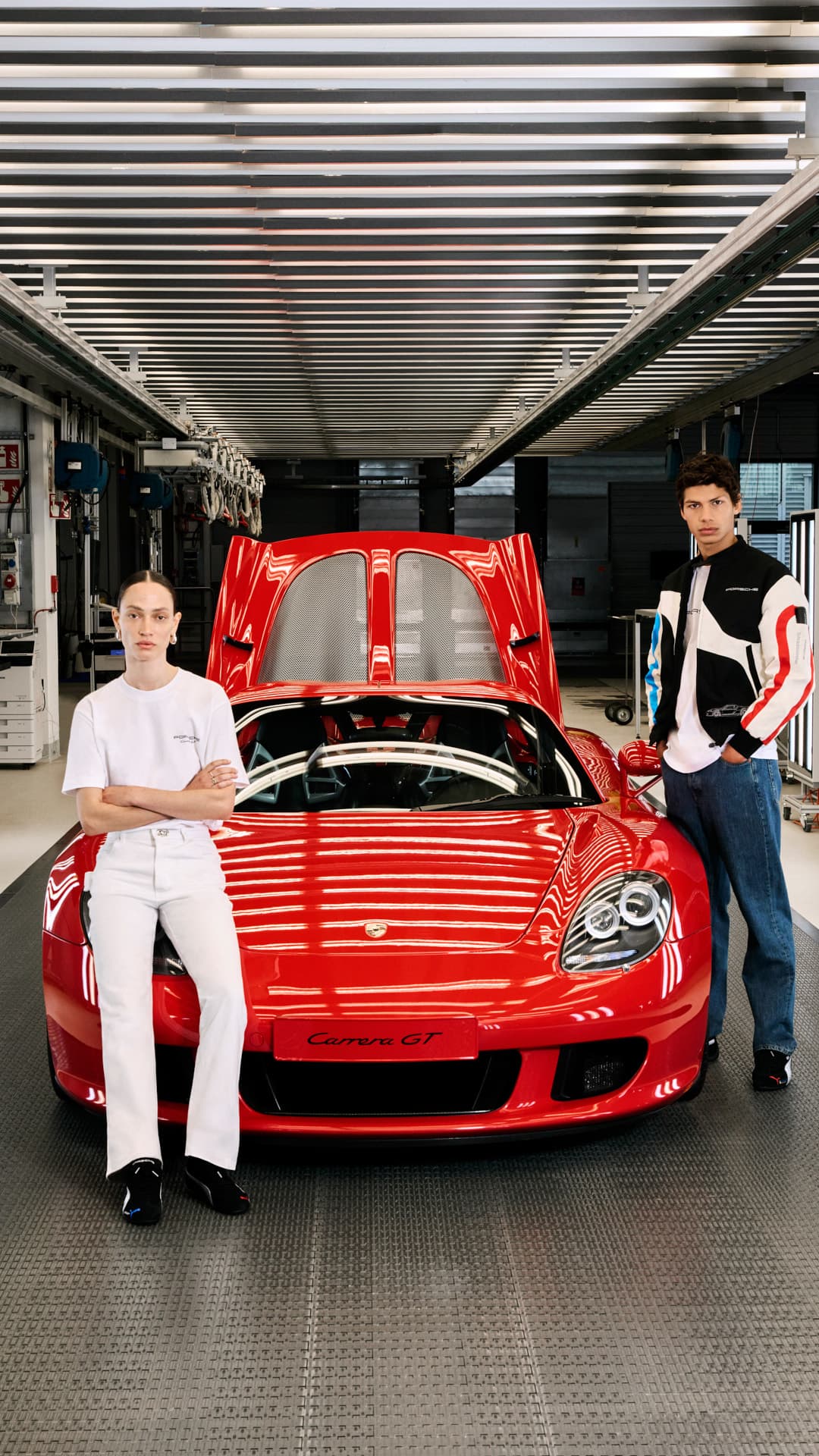 Woman and man wearing the 25 Jahre Porsche Carrera GT Collection standing in front of a red Porsche Carrera GT