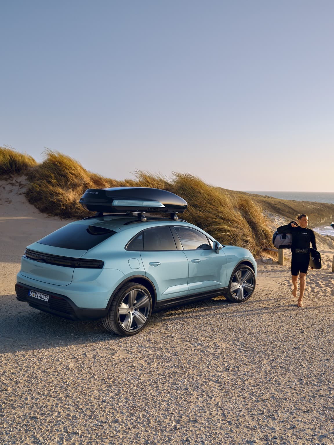 You can see a light blue Porsche Macan at the beach, next to a man