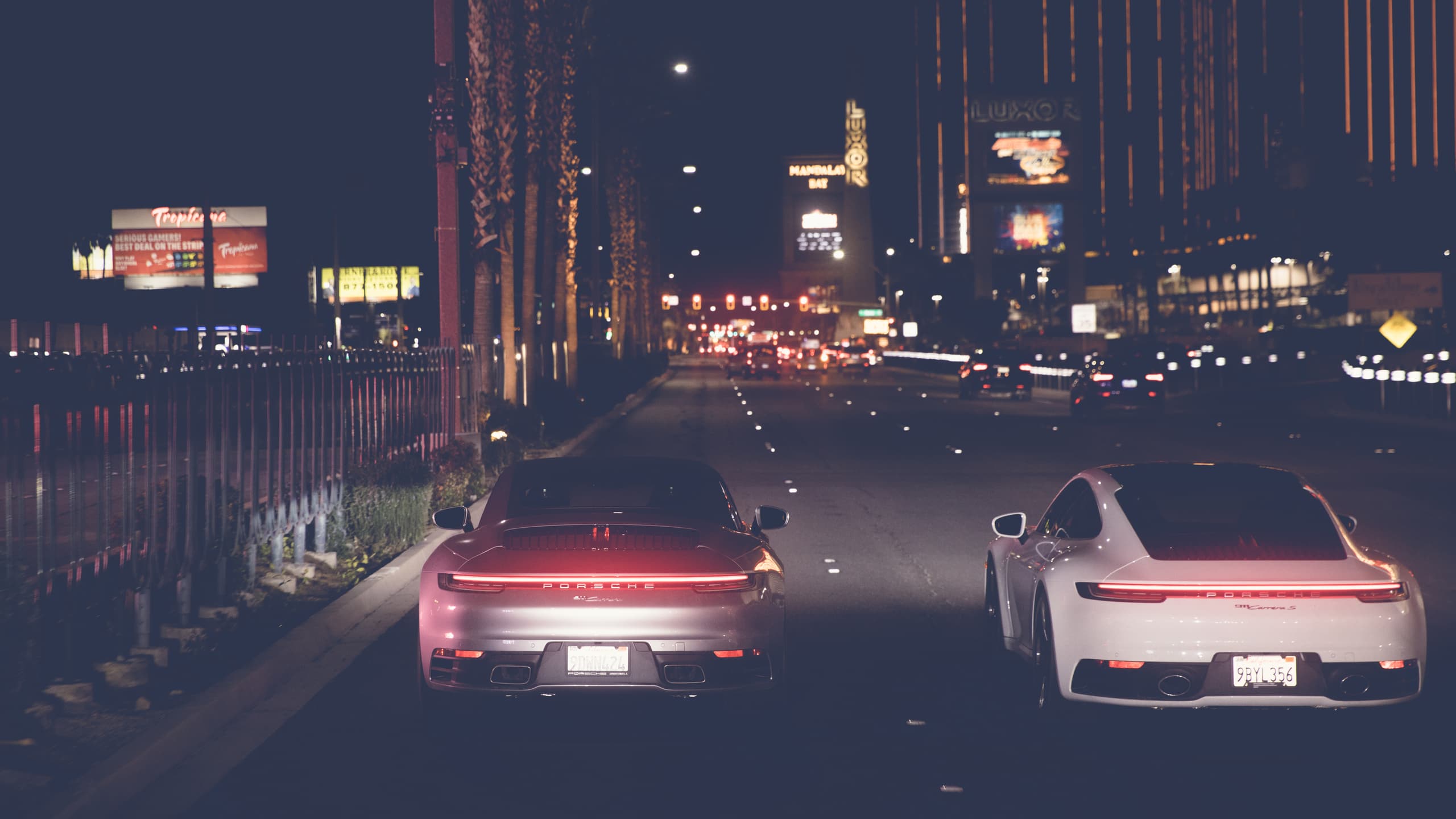 Shown are two Porsche 911s in black and white from behind. They drive at night in an illuminated city.