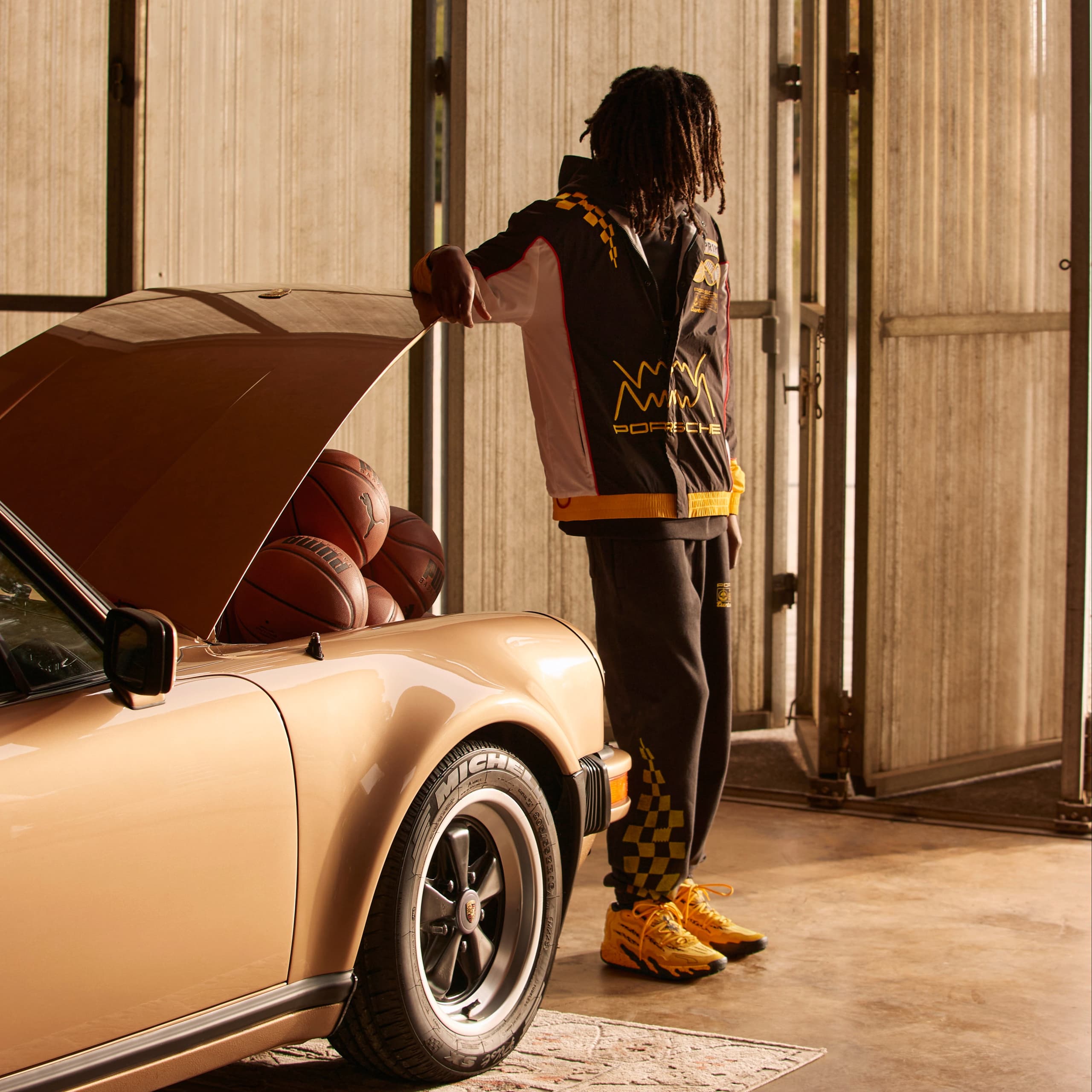 Porsche Puma. Image features man standing in front of a Porsche 911 Turbo, with the front truck open and basketballs inside.
