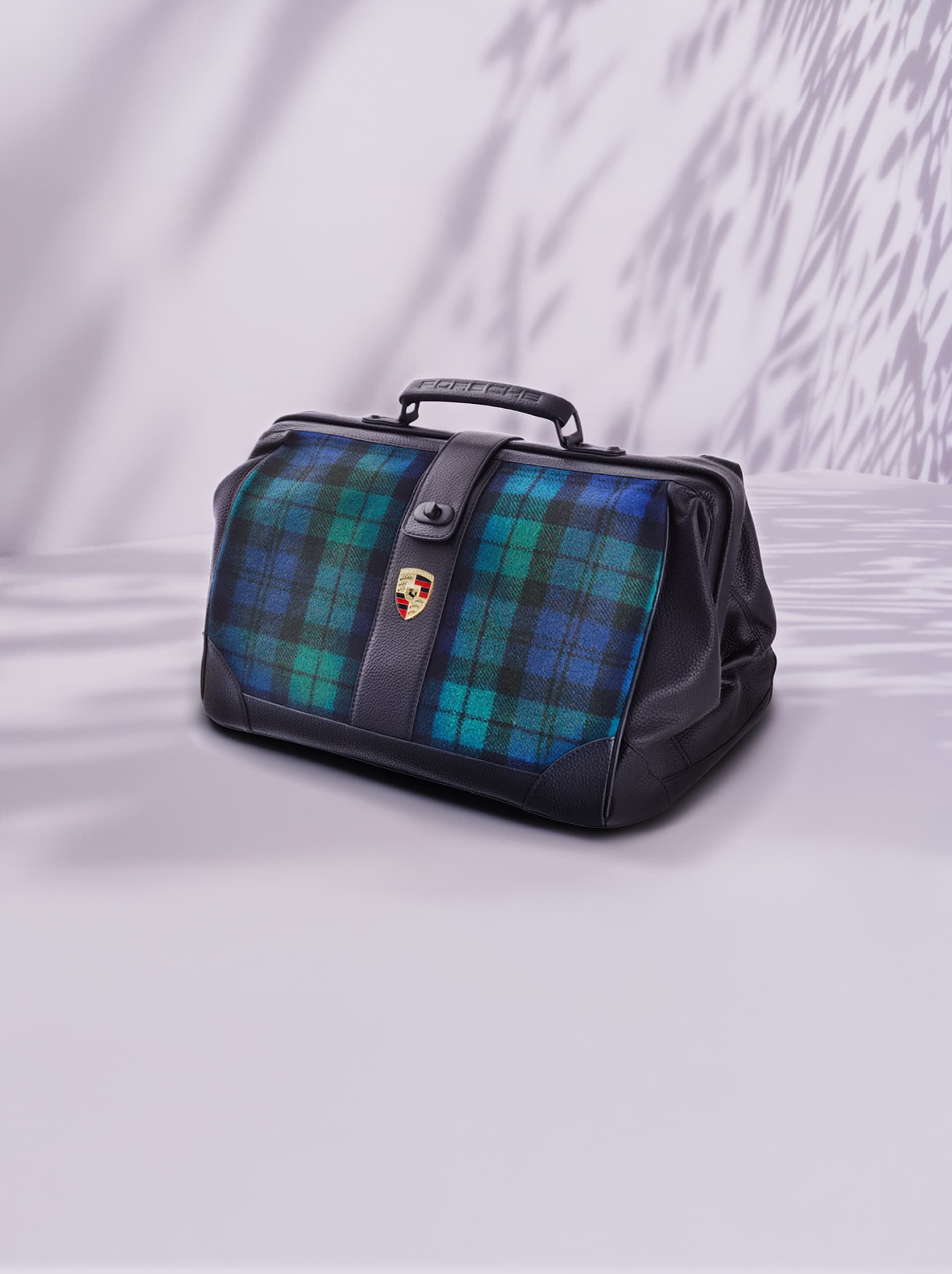 Borsa in pelle nera con motivo a quadri blu-verde, logo Porsche, su sfondo chiaro con ombre.