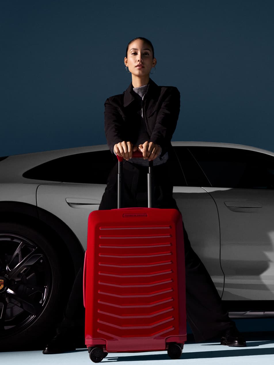 Woman standing with Porsche Design Trolley in red, white Porsche in background