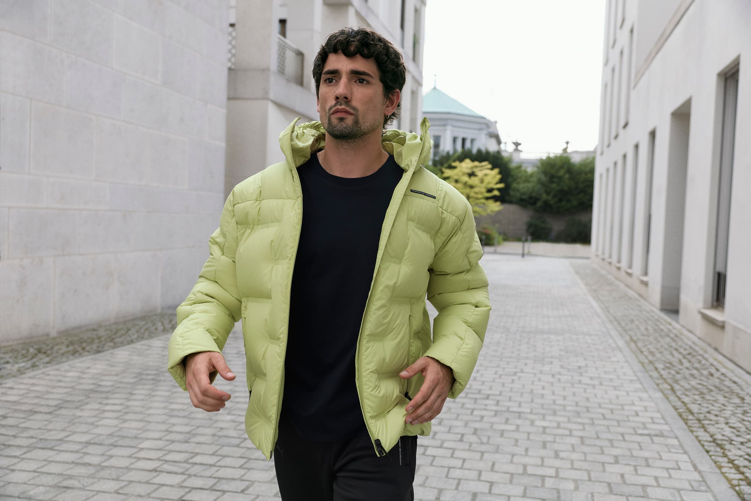 Man in urban setting A sporty young man is running down a street wearing a light green Porsche Design down jacket.