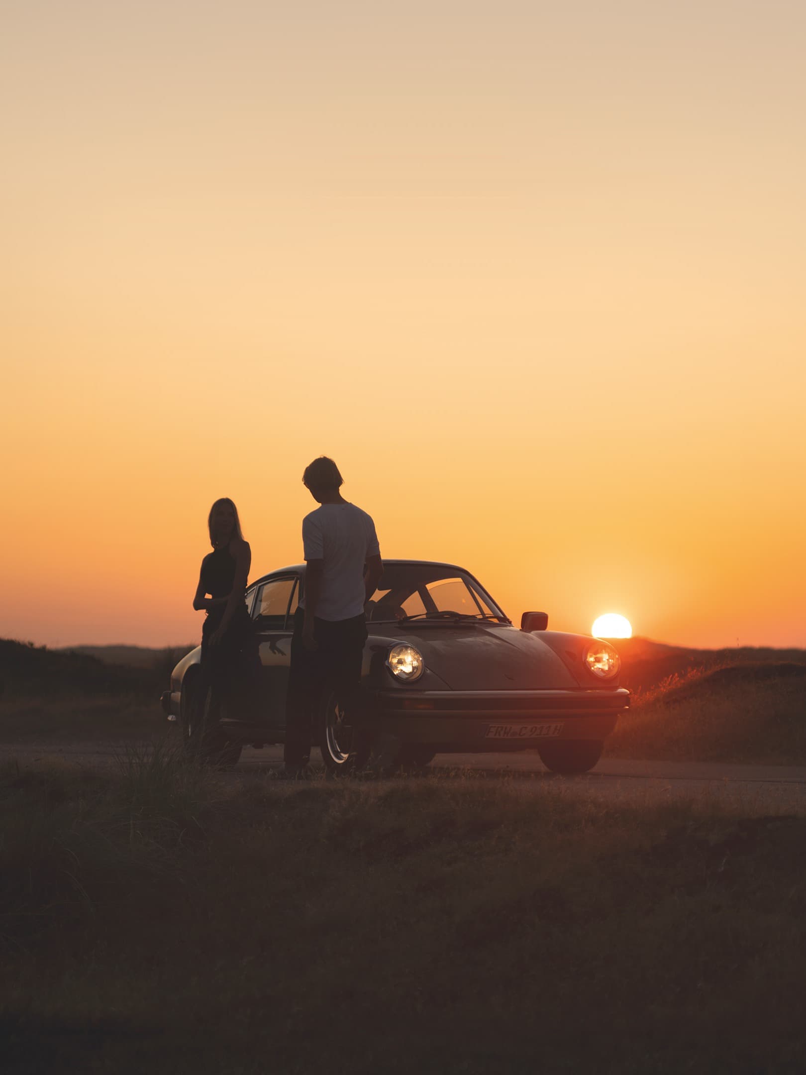 Deux personnes au coucher du soleil, debout devant une 911 classique.