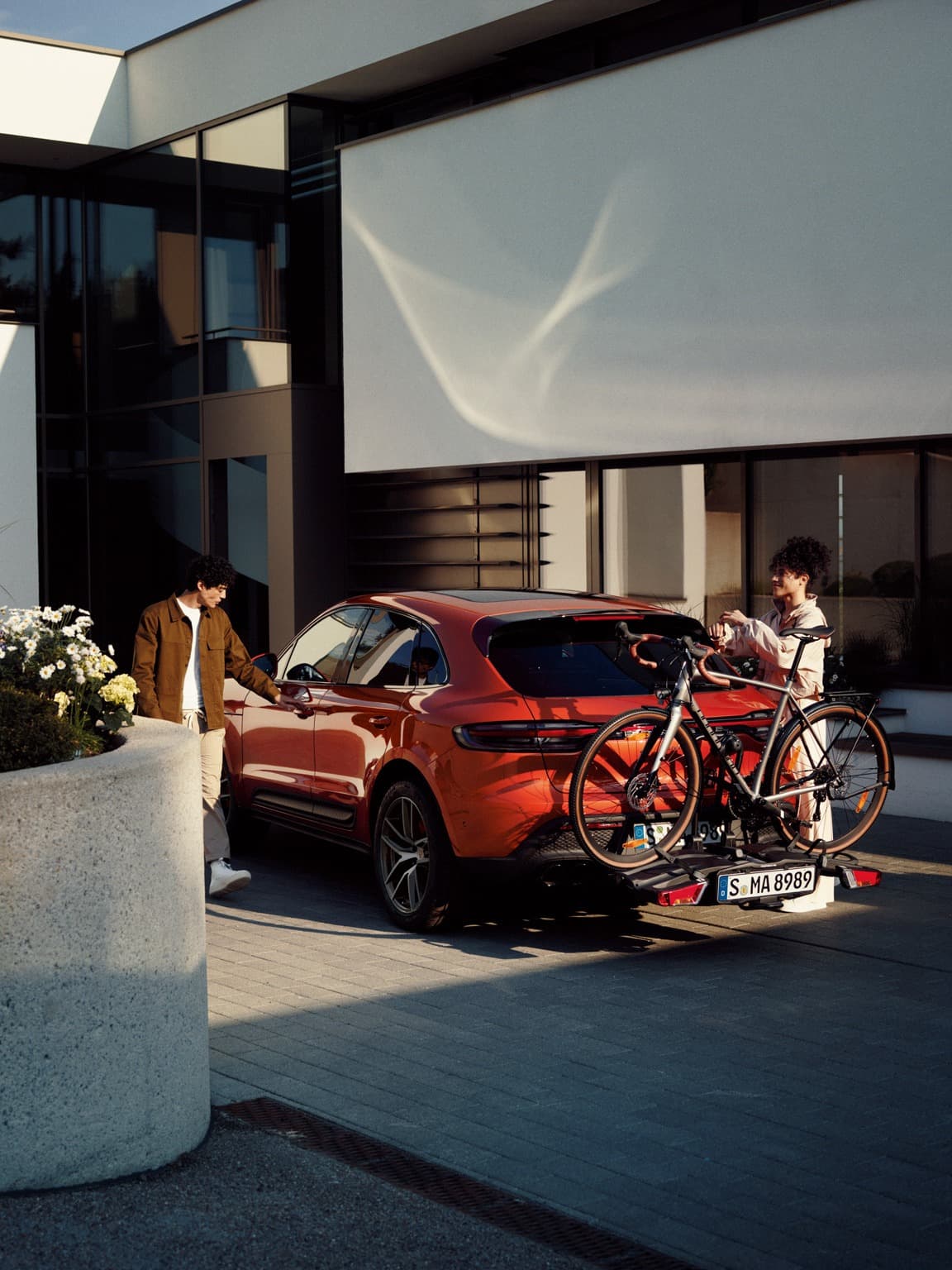 Red Porsche with a bike on the roof, parked on a mountain road, two people nearby, misty peaks in the background.