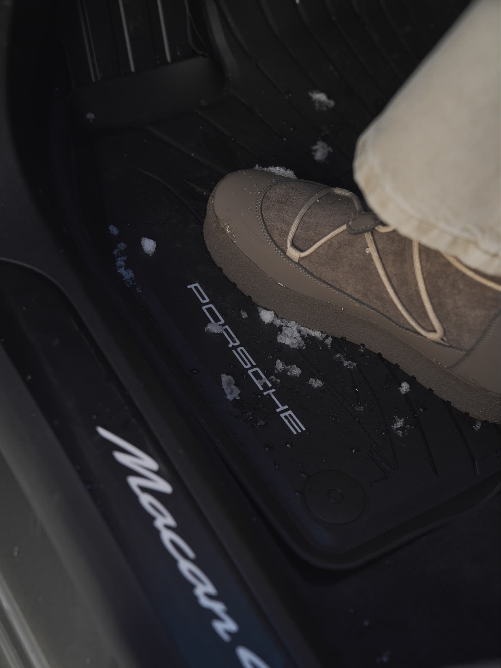 Fuß in beigem Stiefel auf Porsche Macan Fußmatte mit Schnee, zeigt Innenraumdetails und Winterkontext.