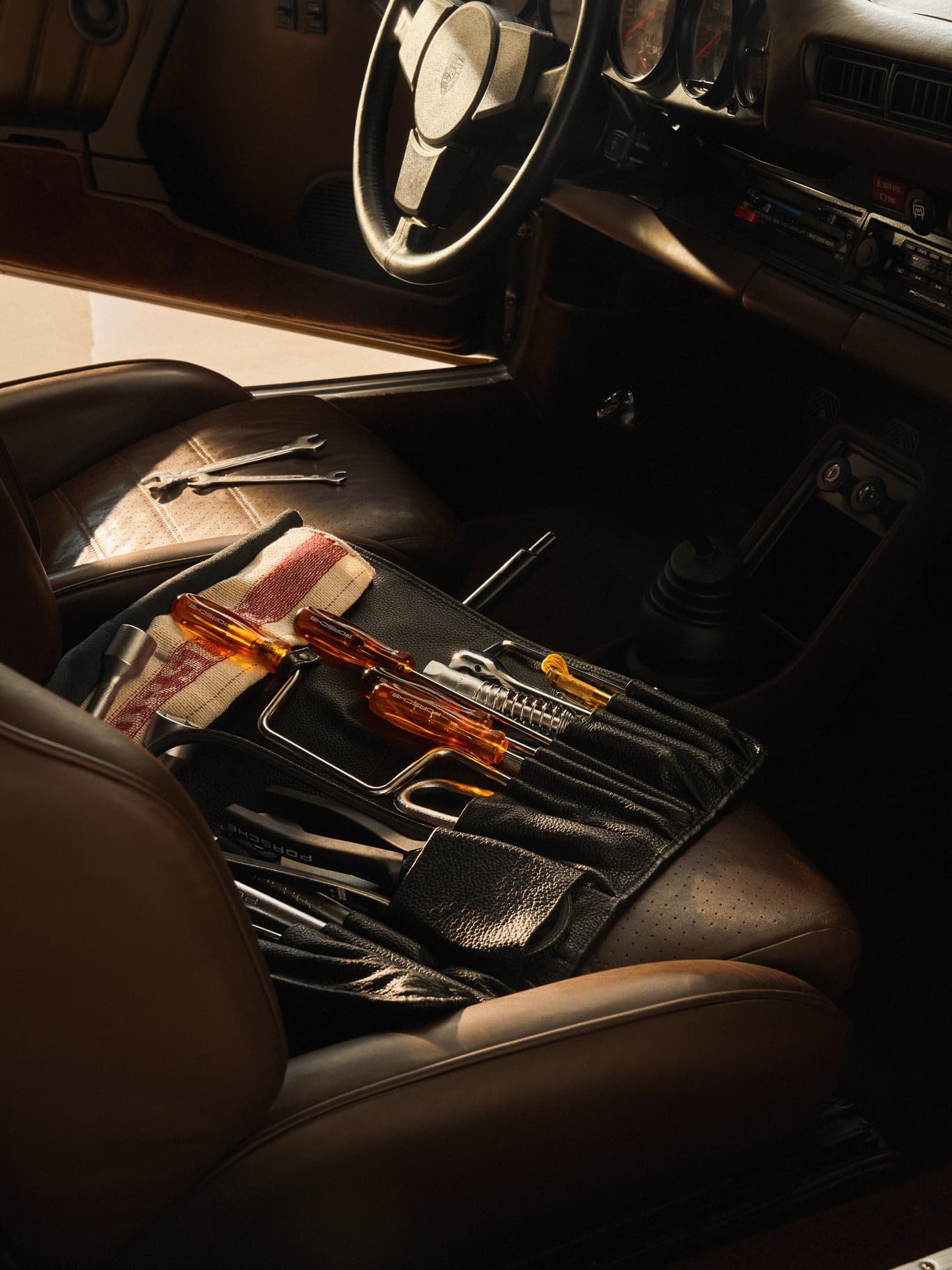 Tool kit with orange handles on brown leather car seat, inside a vintage Porsche with a black steering wheel.