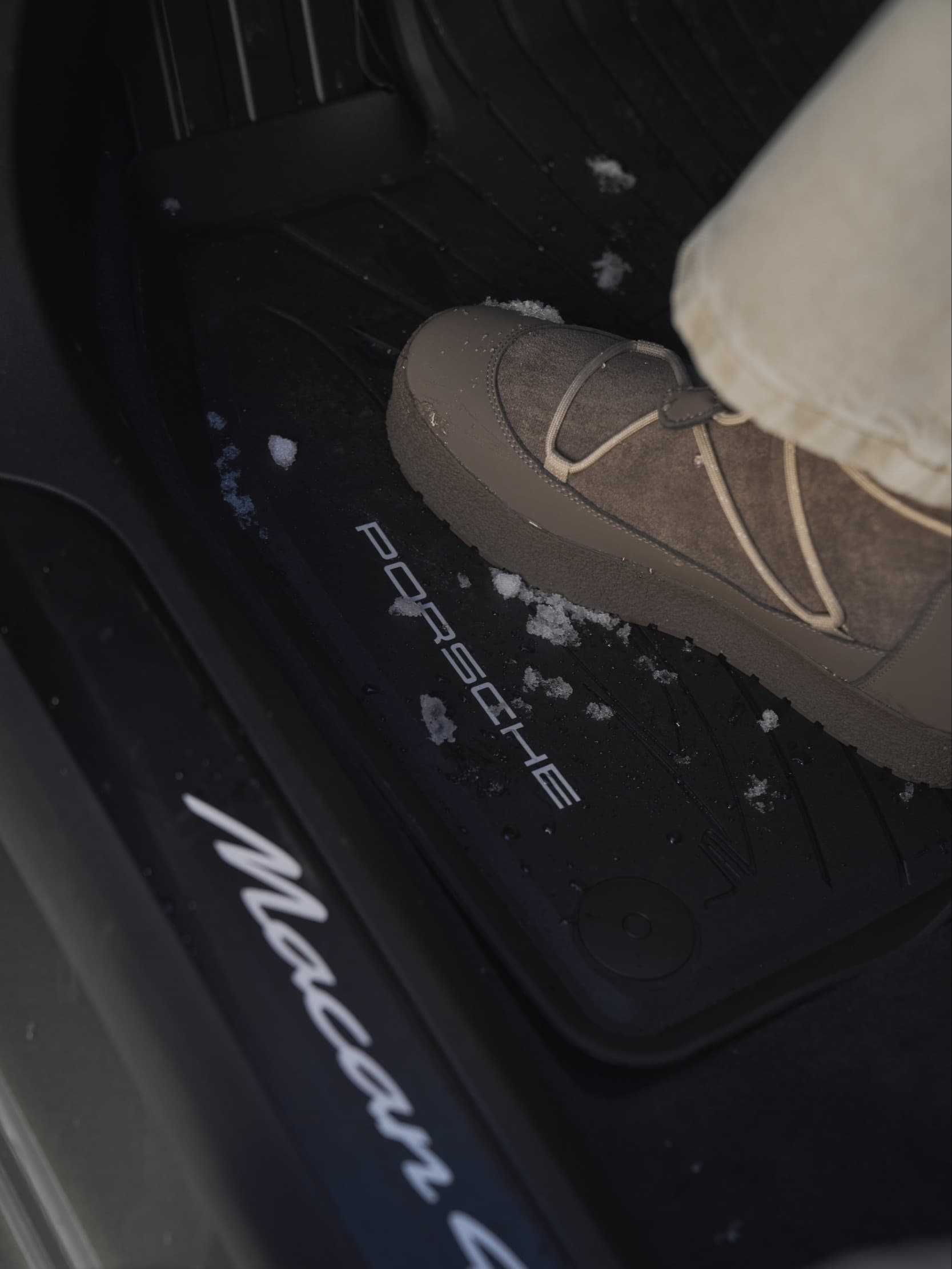 Foot in beige boot on Porsche Macan floor mat with snow, highlighting interior detail and winter context.