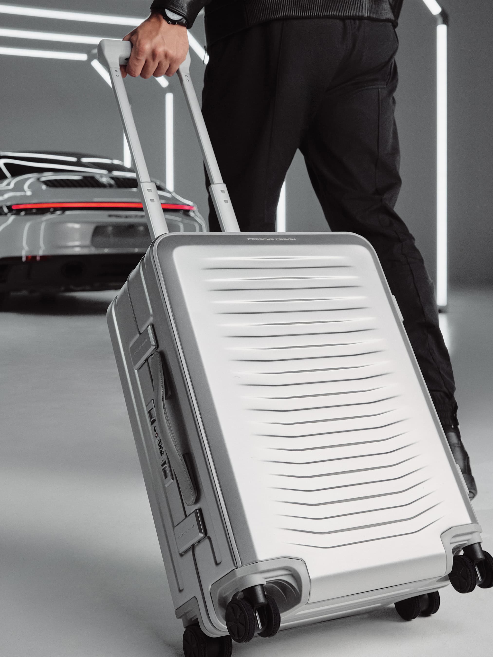Porsche Design Maleta de aluminio carreid por un hombre a un 911
