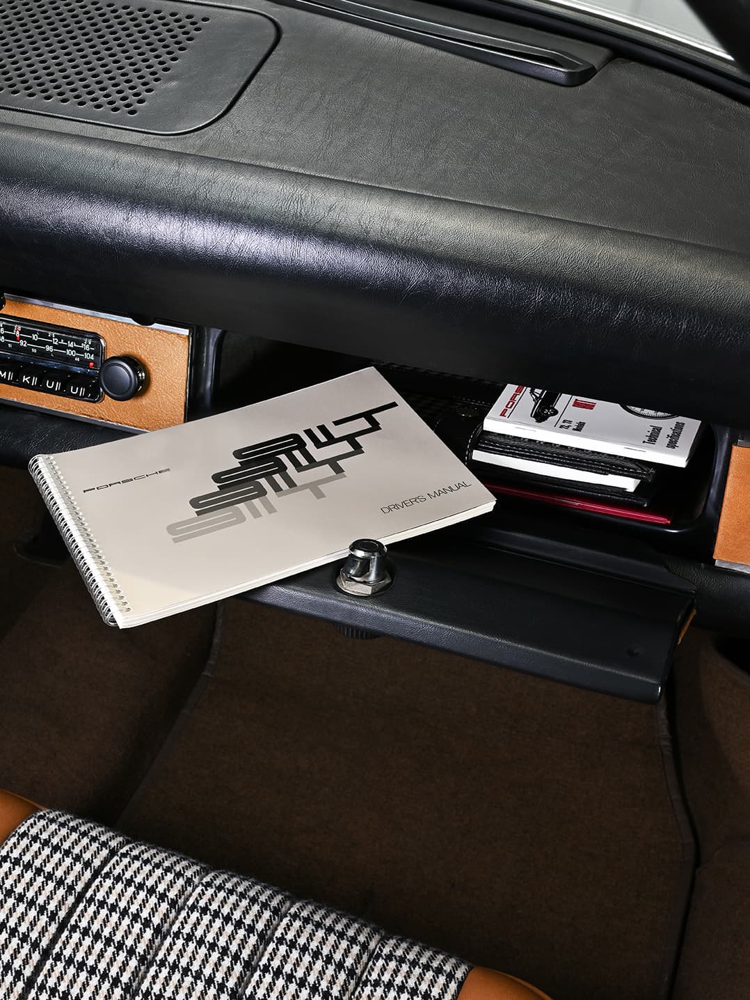 Åpen hanskerom med Porsche-manual og dokumenter inni, svart skinn-dashbord, vintage radio, hundetannmønstret sete.
