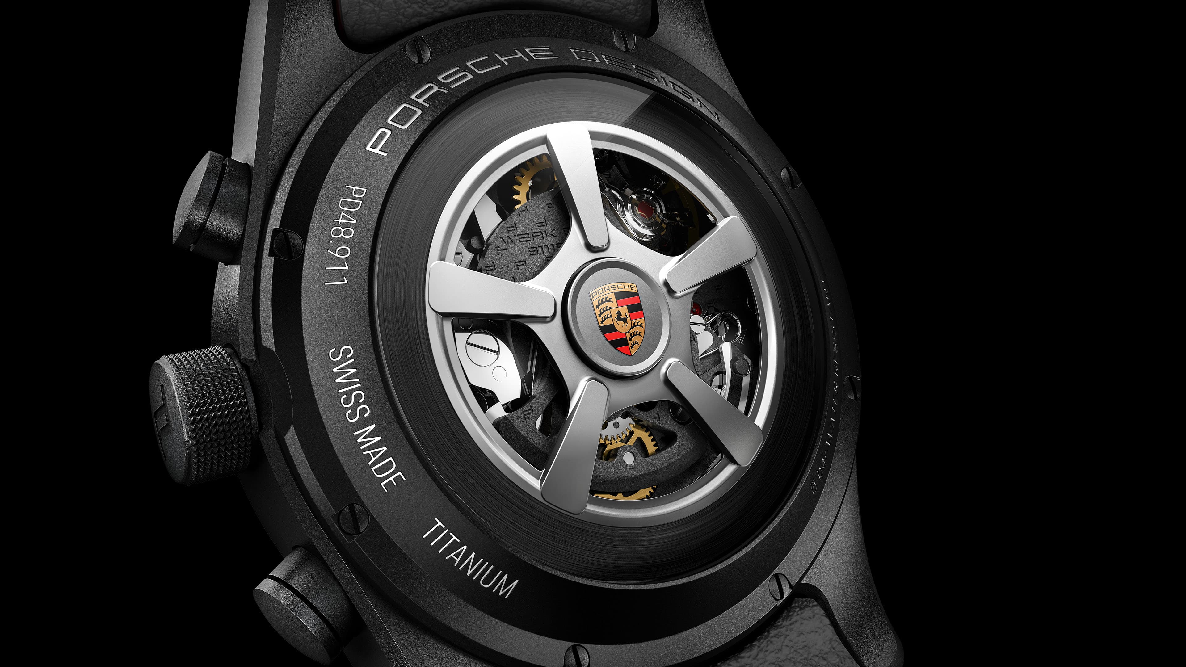 A close-up of the back of a black Porsche Design watch featuring a see-through case back, a rotor with a wheel-spoke design, and the Porsche crest.