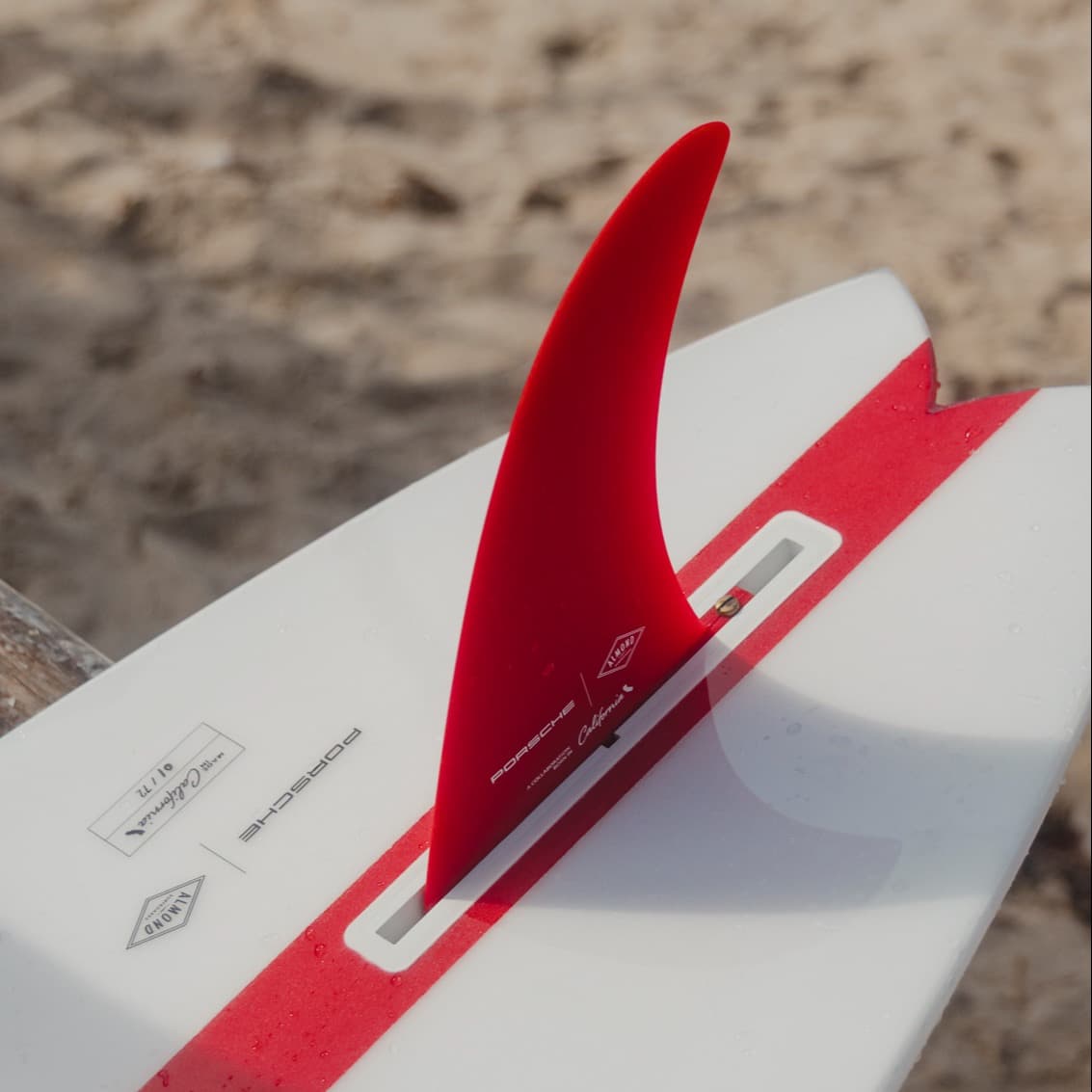 White surfboard with red stripe and fin
