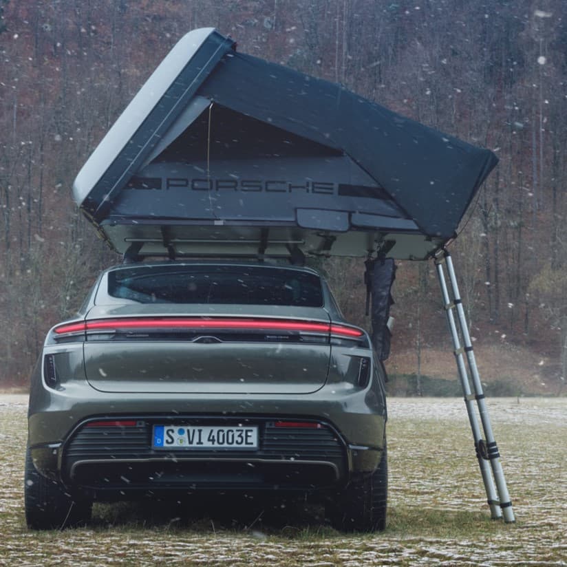 Voiture Porsche avec tente de toit dans un champ enneigé, vue arrière, forêt en arrière-plan, échelle attachée à la tente.