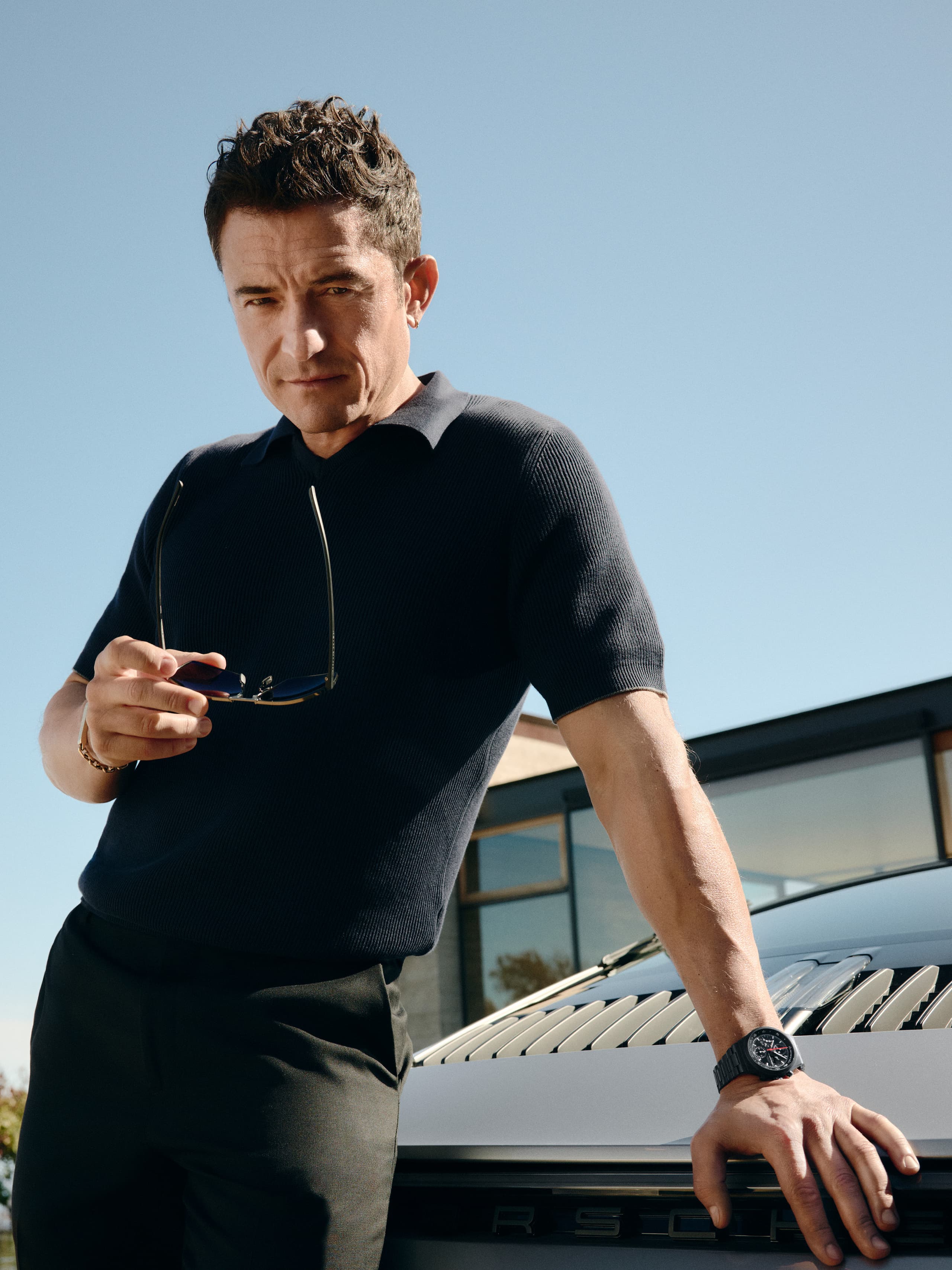 Orlando Bloom ma na nadgarstku zegarek Chronograph 1 – All Black Numbered Edition, oparty o tył samochodu Porsche.