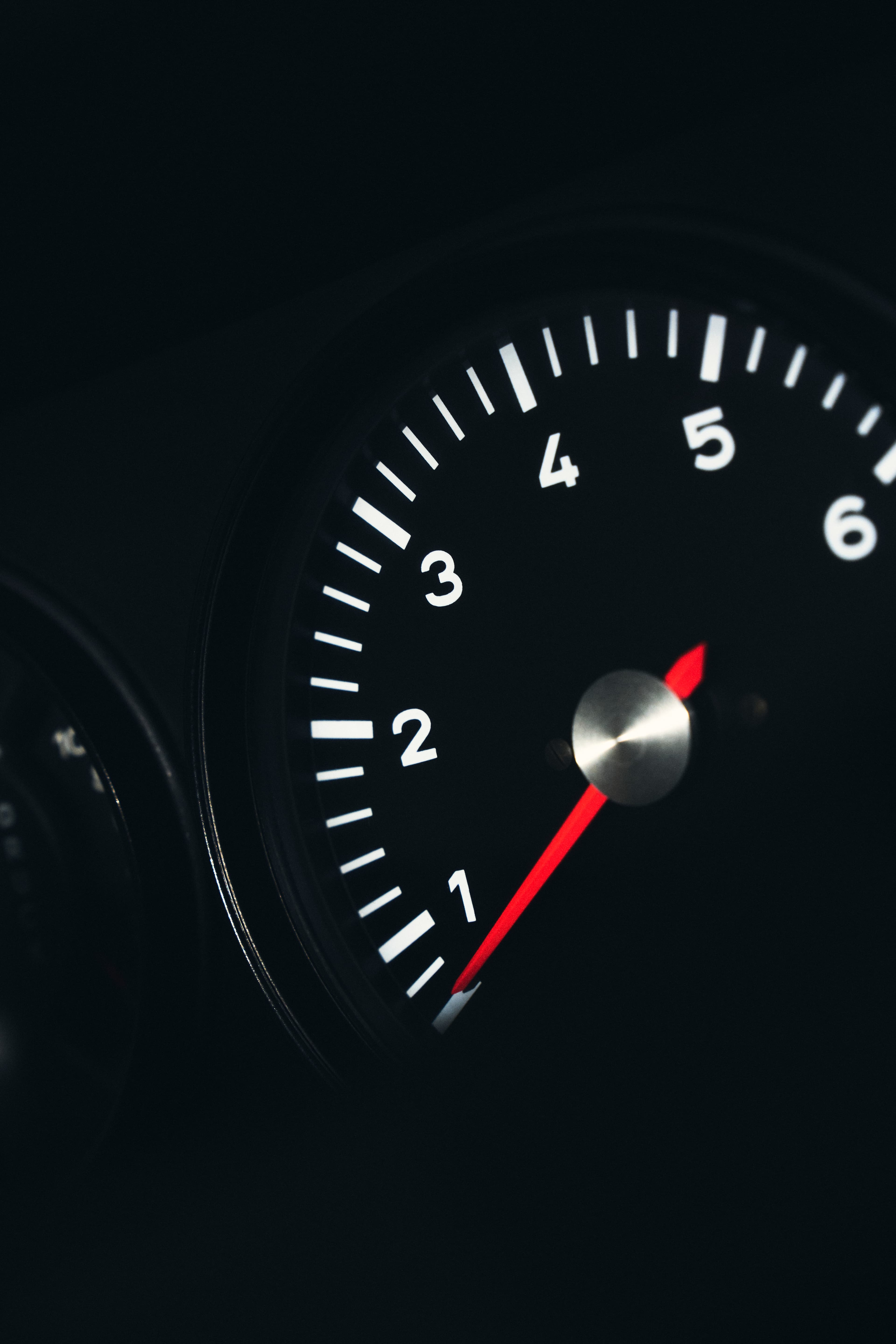 Close-up of black tachometer dial with white markings and red needle, showing numbers 1 to 6.