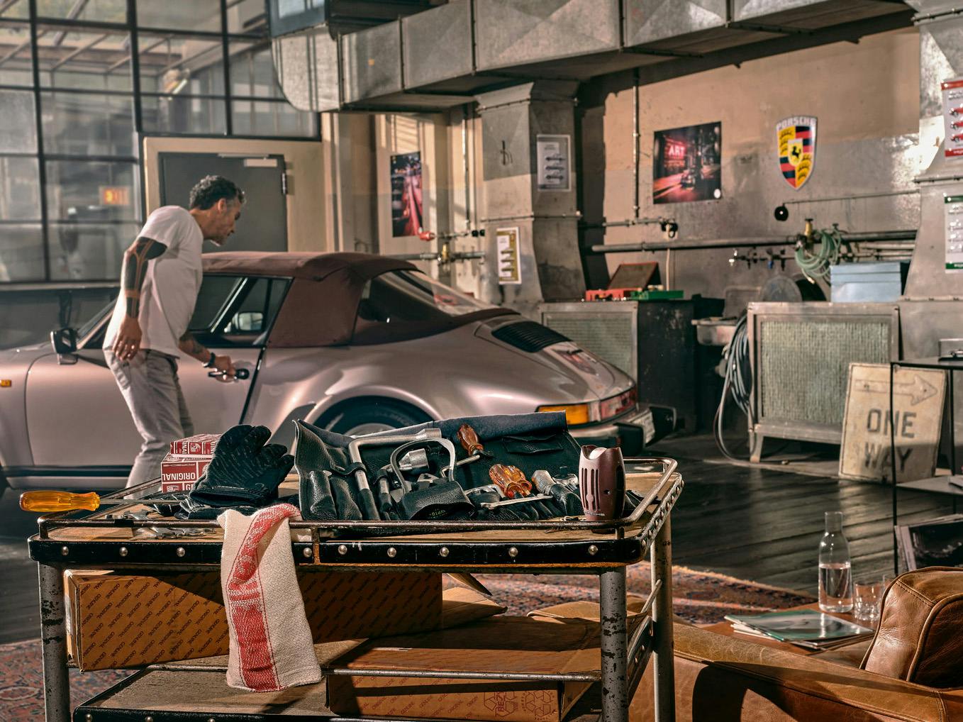 Shown is a detail of a Soul Garage with a man opening his silver vintage Porsche car in the background and a Porsche tool bag in the foreground.