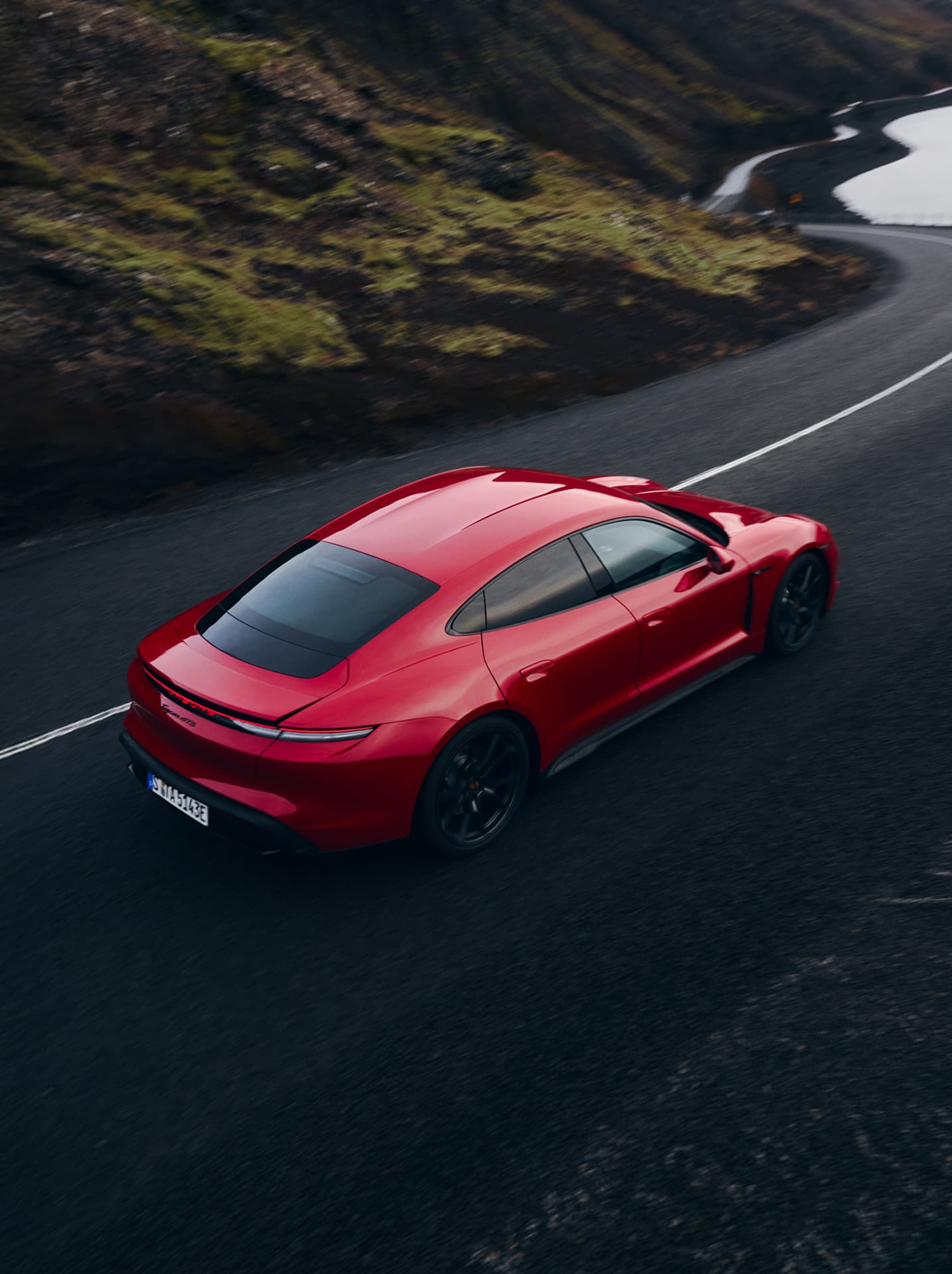Roter Porsche auf einer kurvenreichen Straße, umgeben von rauer Landschaft und Grün.