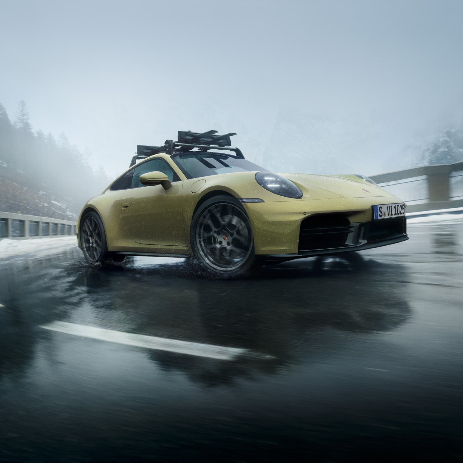 Gelber Porsche 911 mit Dachgepäckträger auf nasser Bergstraße, nebliger Hintergrund, bewölkter Himmel.