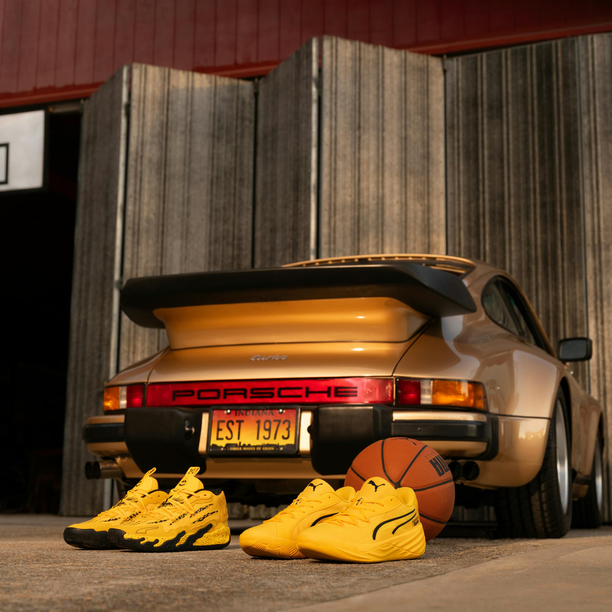 The image features a yellow Porsche Turbo car. It is parked in front of a building and has Porsche x Puma basketball shoes featured in the photo.