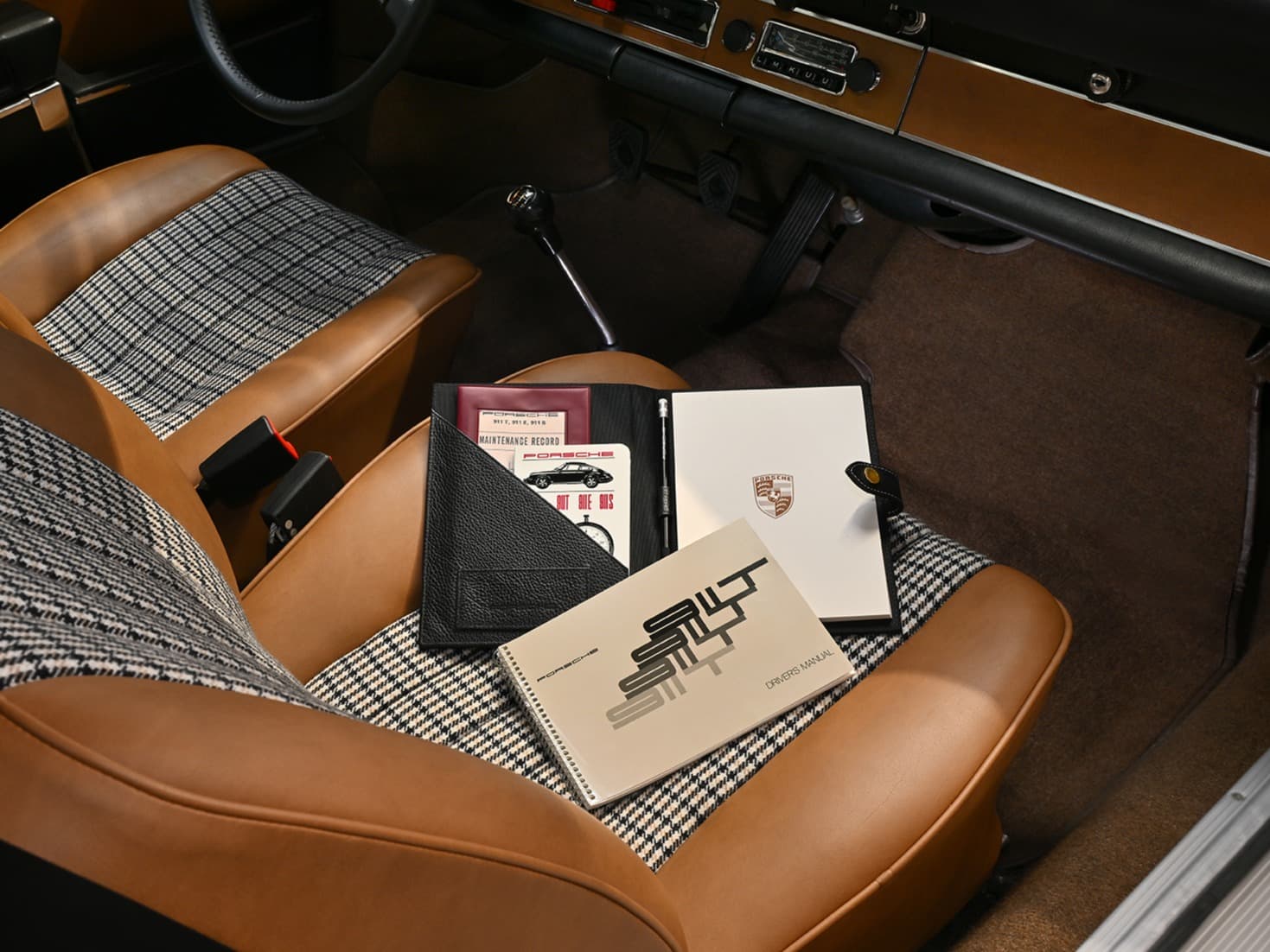 Porsche car interior with tan leather and houndstooth seats, manuals and document folder on passenger seat
