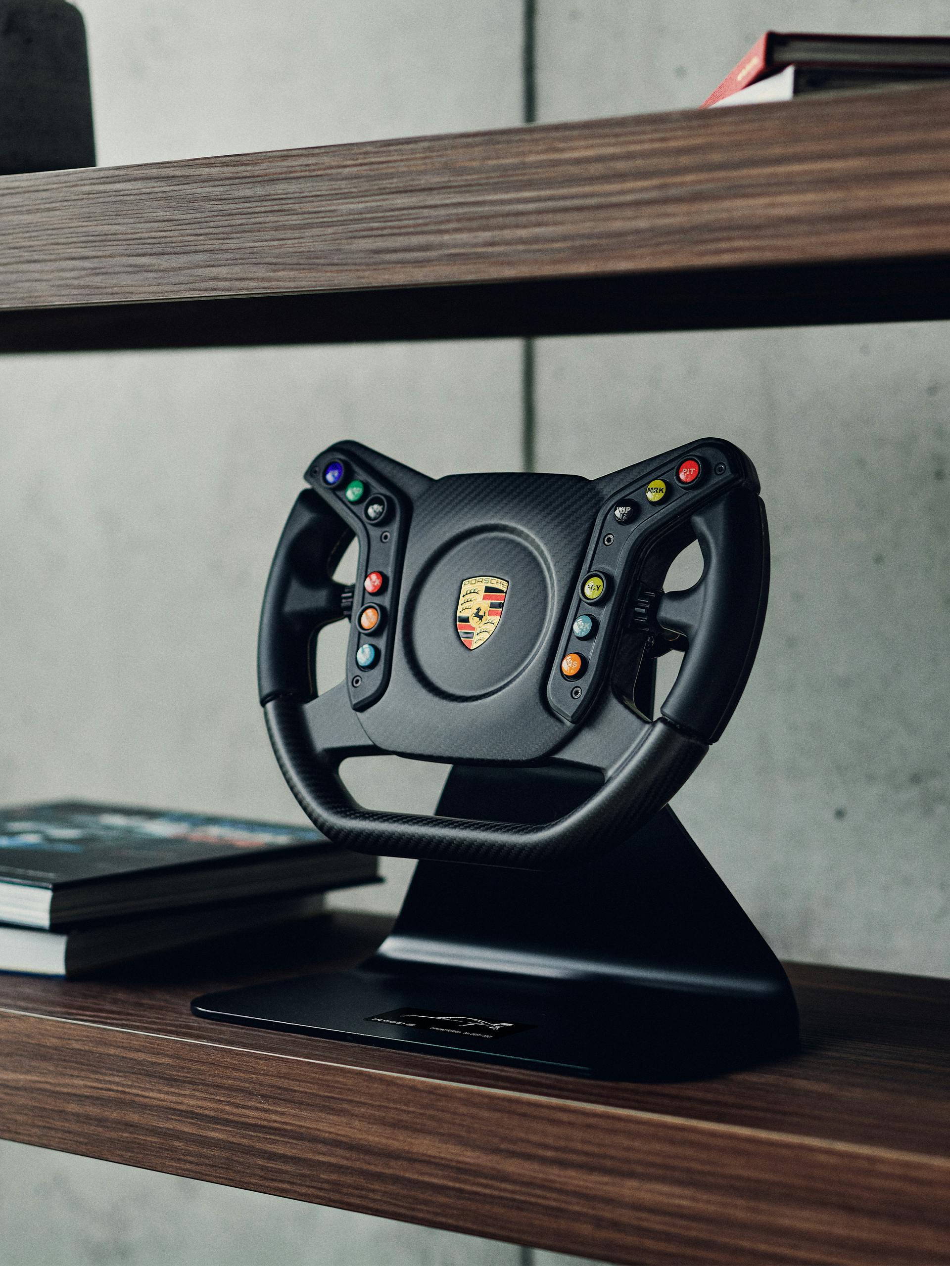 Pictured is the new Porsche Gaming steering wheel in black on a brown wooden shelf.