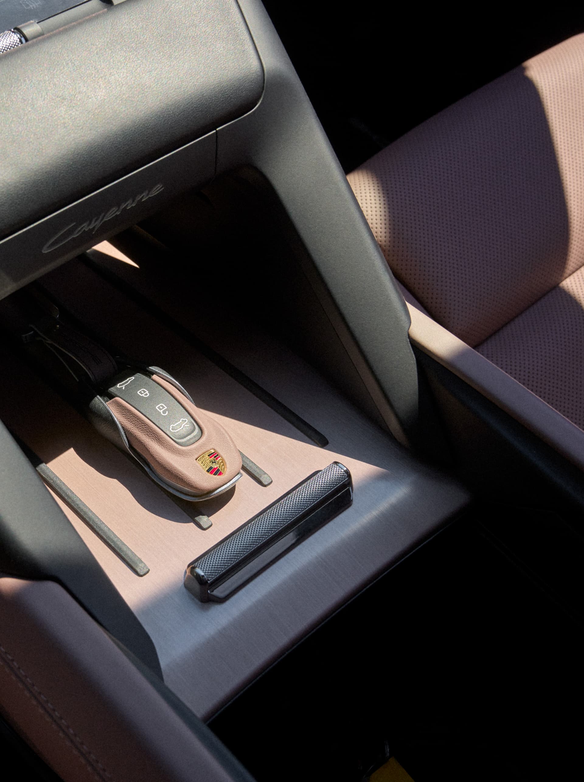 Porsche car interior with brown leather key fob on brushed metal center console beside perforated leather seat