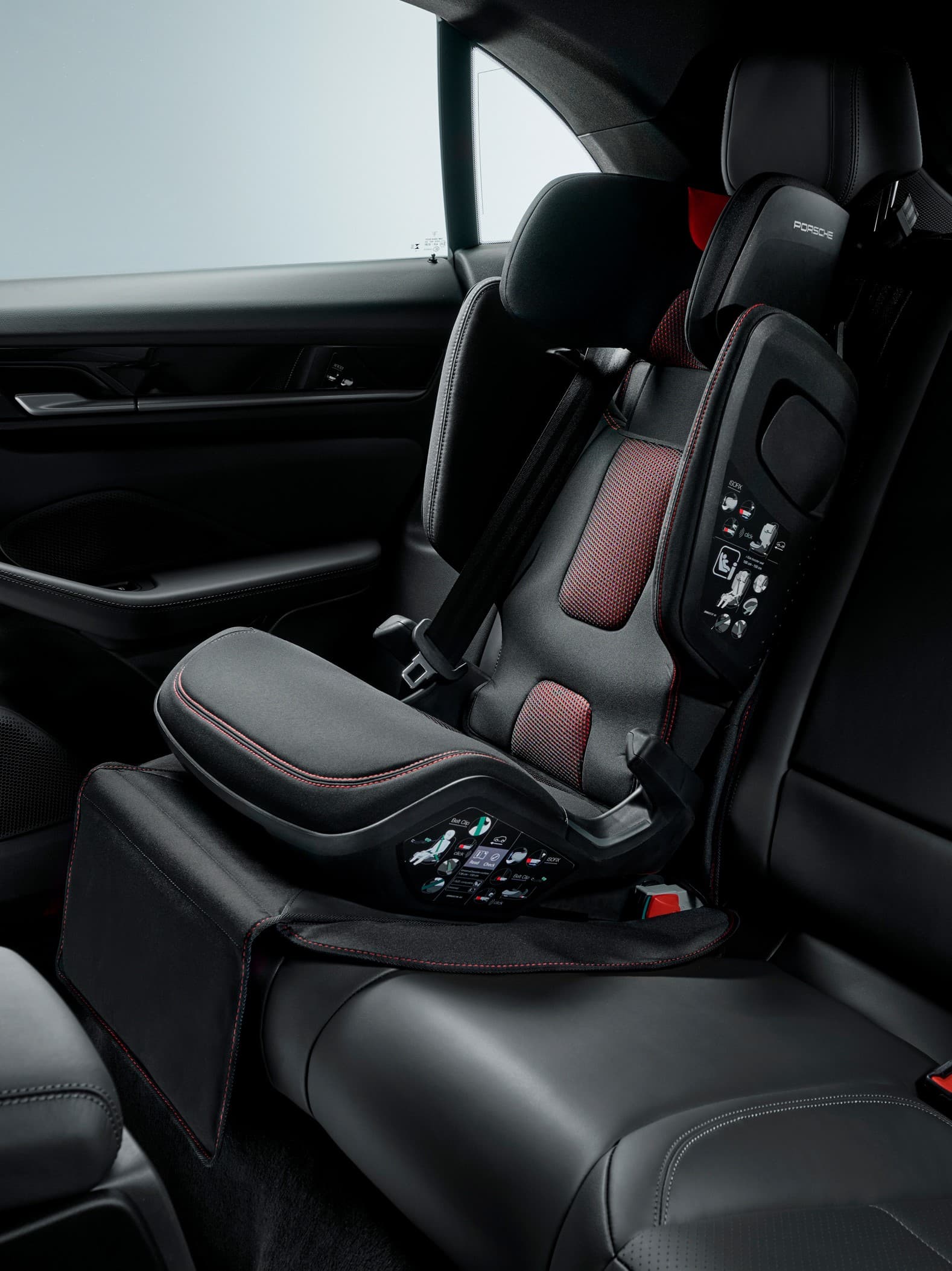 Black and red Porsche child seat in a car's rear seat, featuring safety harness and side protection.