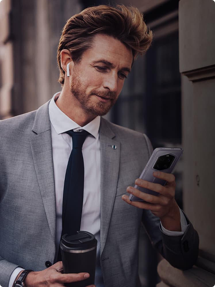 Businessman in a gray suit and headphones in his ear holds the PORSCHE DESIGN HONOR Magic7 RSR in his hand