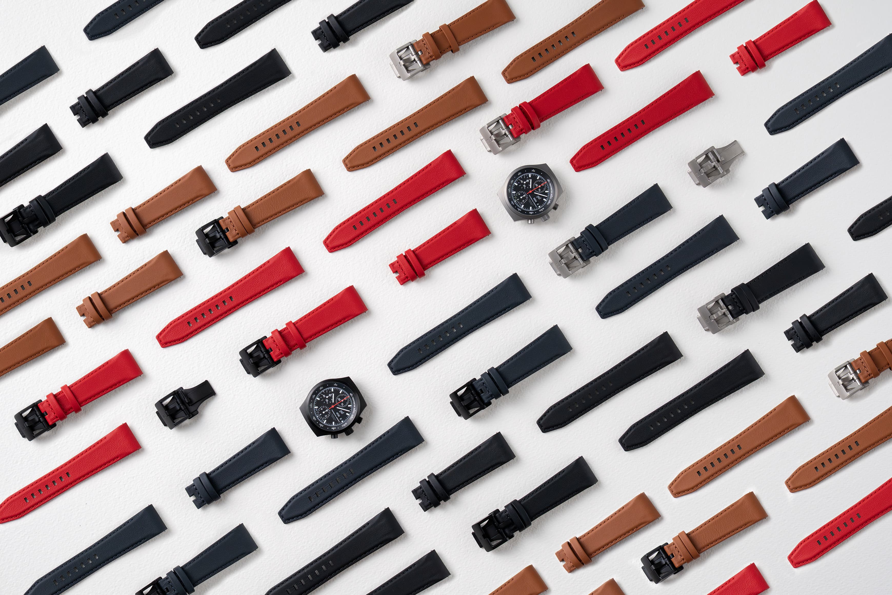 Various watch straps in black, brown and red on a white background, with two chronograph watches.