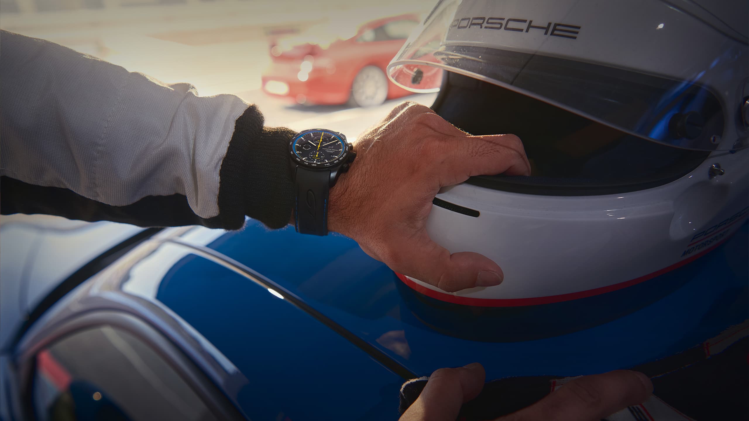 Mężczyzna ma na sobie czarny zegarek na rękę Porsche 911 GT3 Touring i trzyma kask motocyklowy.
