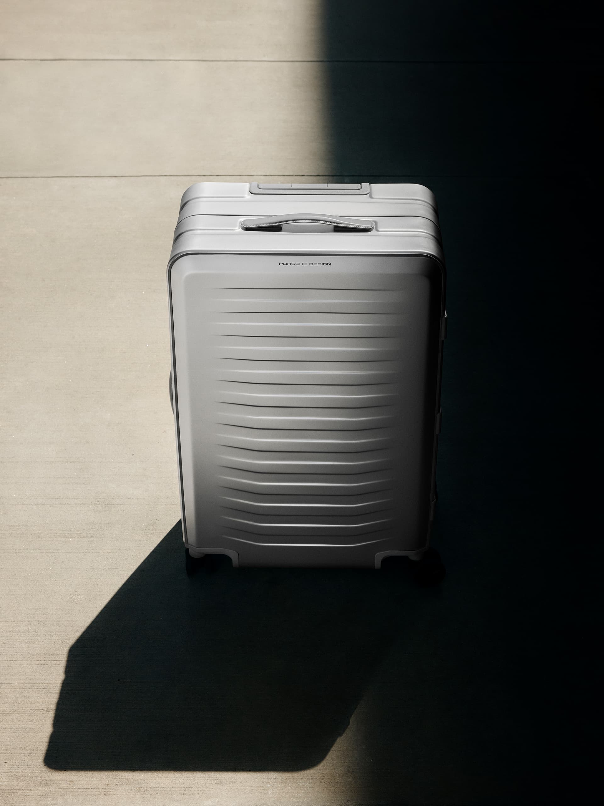 Silver suitcase with textured design, standing on a concrete floor, partially in shadow.