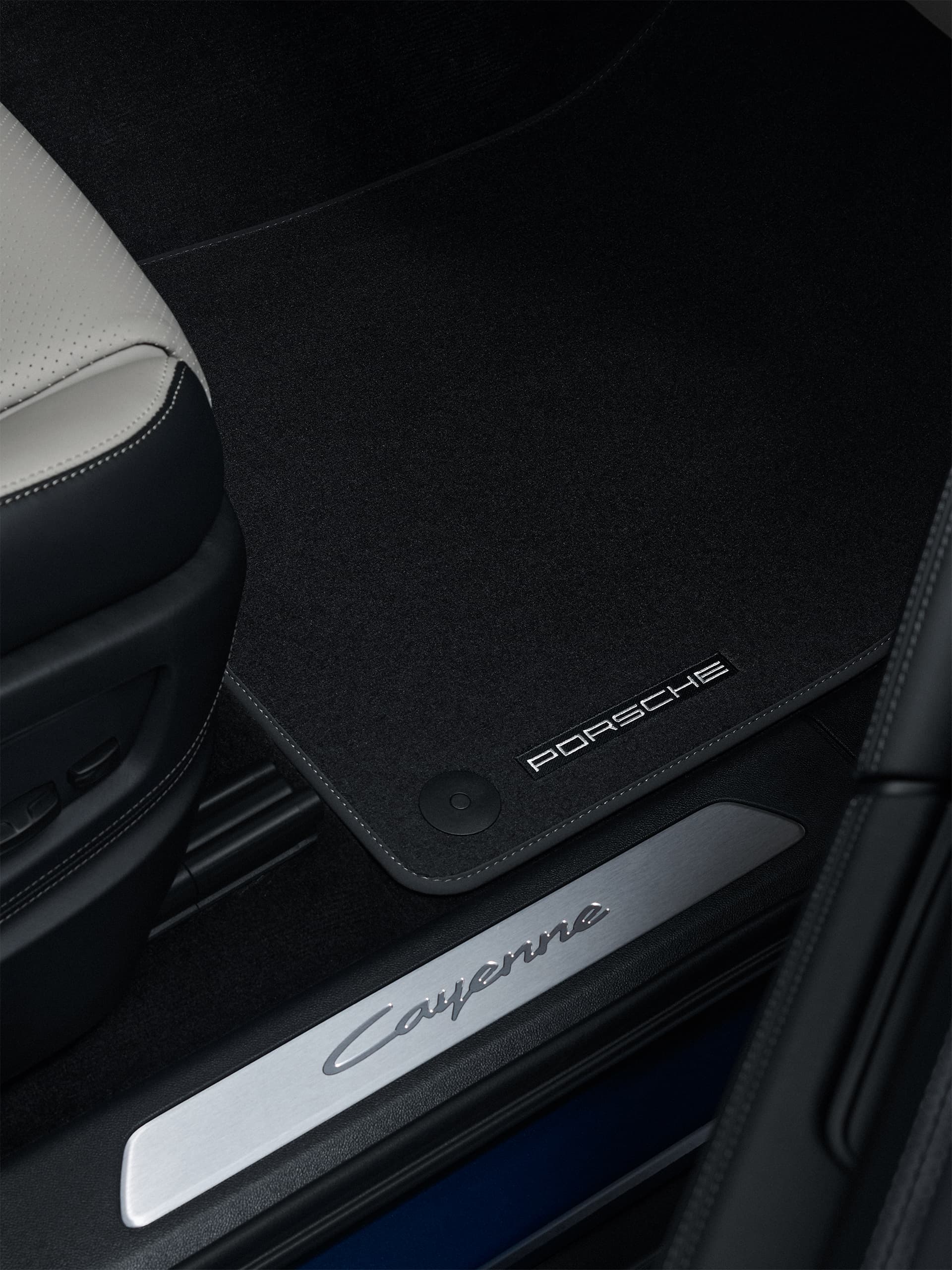 Tapis de sol noir Porsche dans un Cayenne, avec lettrage PORSCHE brodé à côté de la baguette de seuil de porte « Cayenne ».