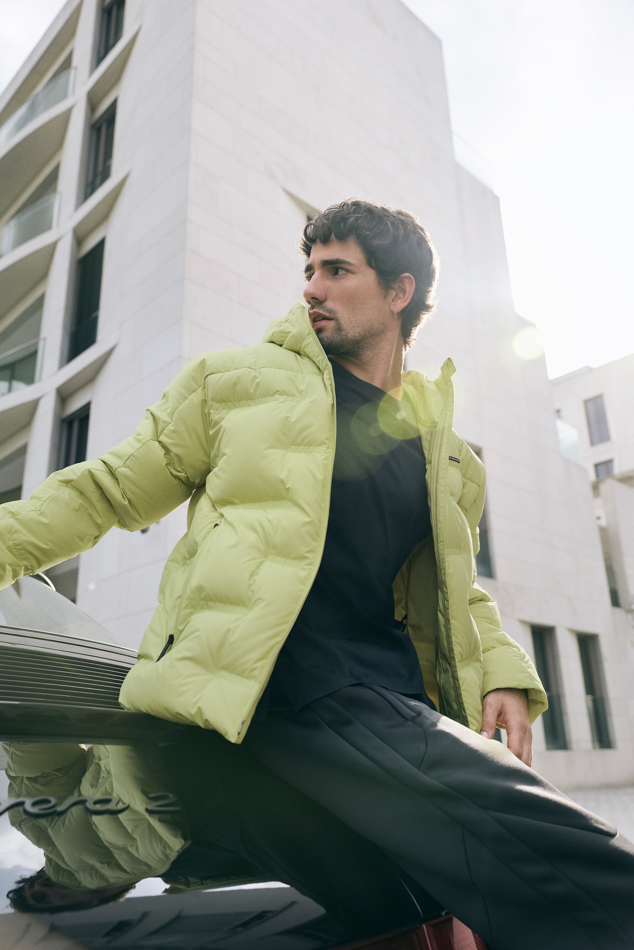 Man in urban setting A sporty young man is running down a street wearing a light green Porsche Design down jacket.