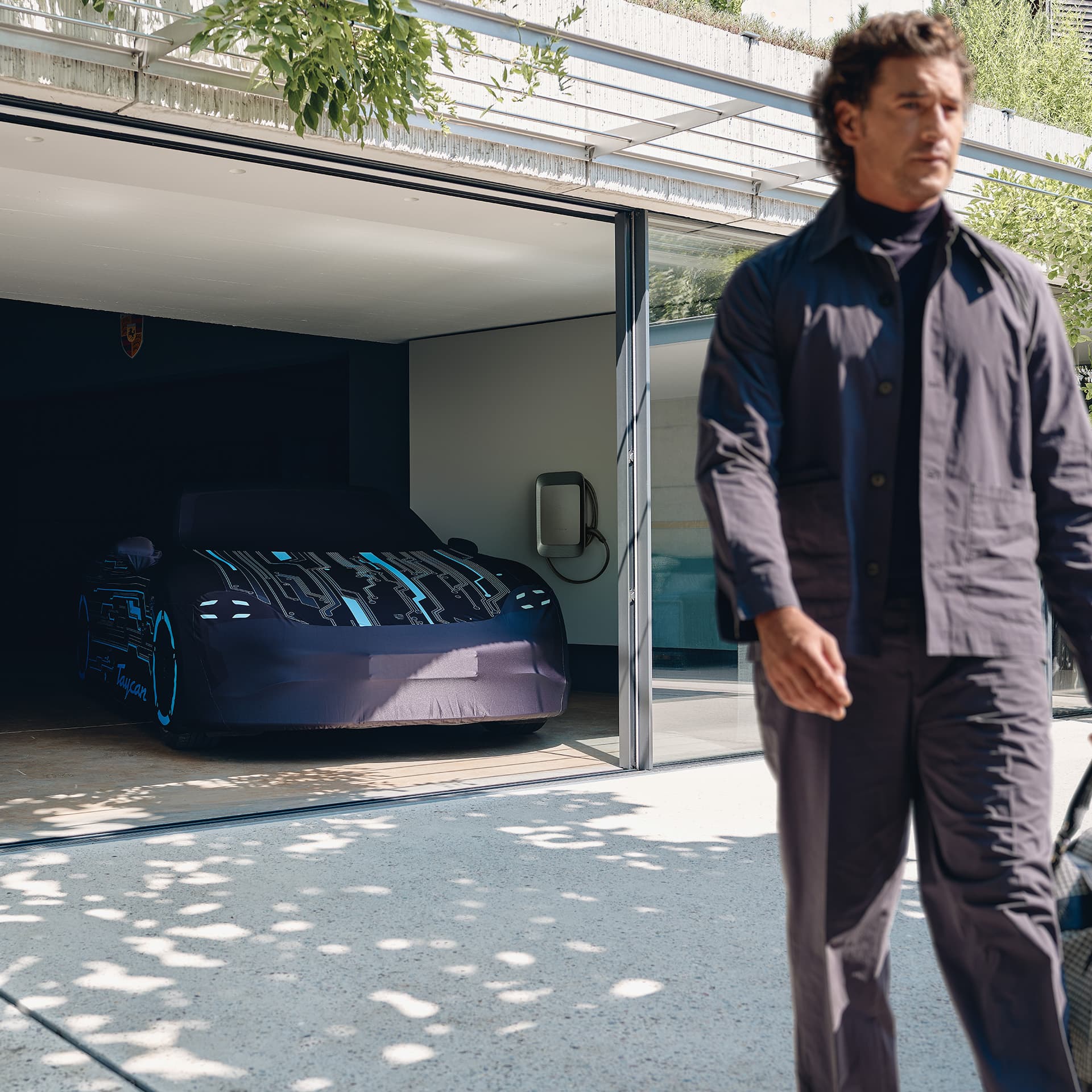 Man pushes his Porsche eBike in front of his garage with two historic Porsche 911s