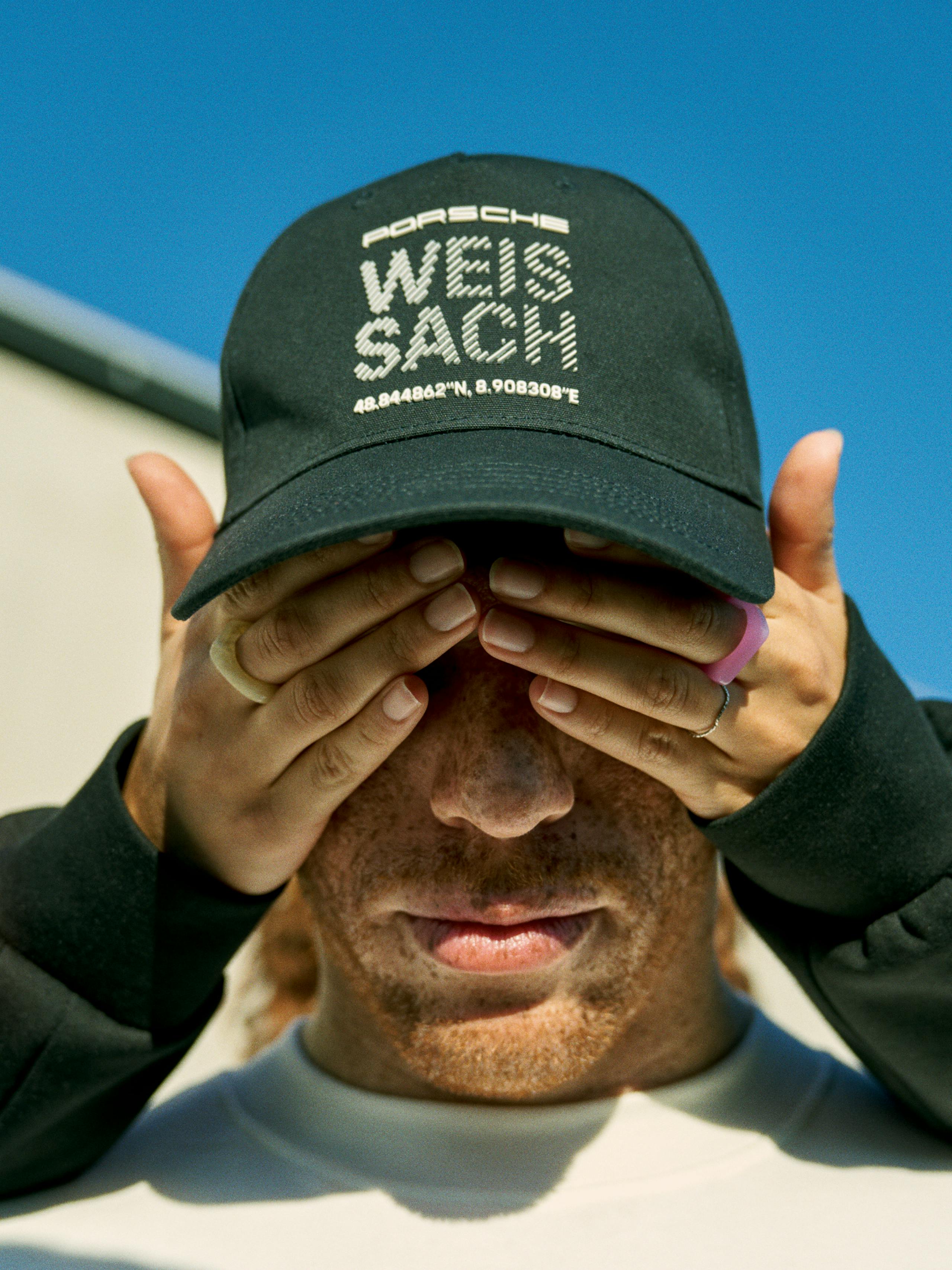 You can see a man with a cap and the white lettering "Weissach". The man's eyes are kept from behind.