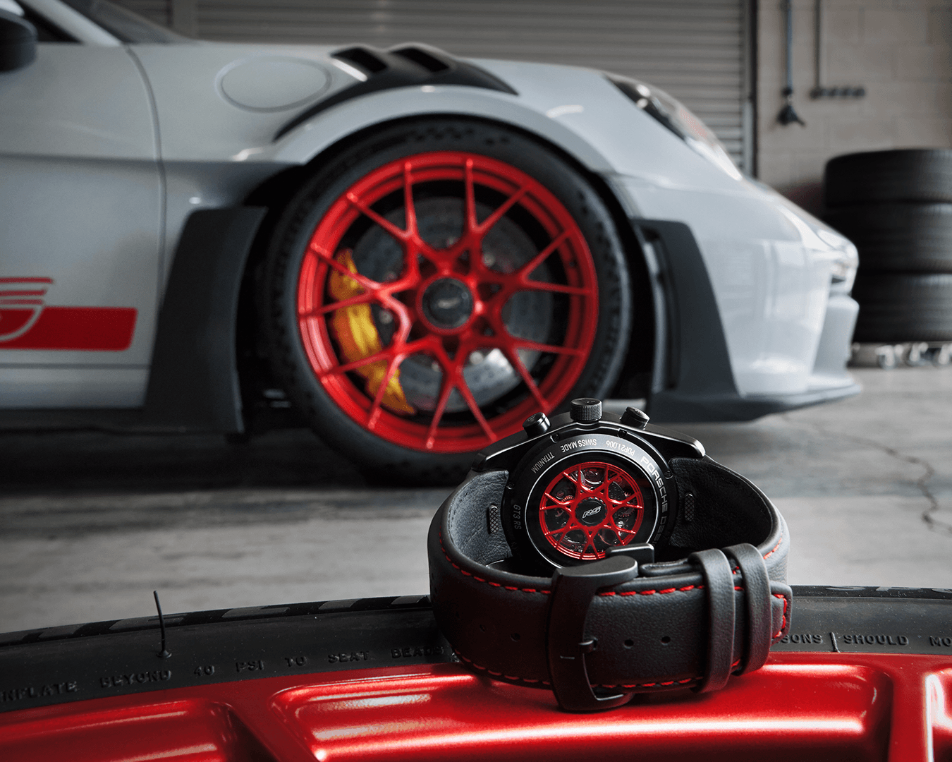 The Chronograph 1 GT3 RS wristwatch is shown from behind and in the background is a Porsche 911 GT2 RS in white with red details