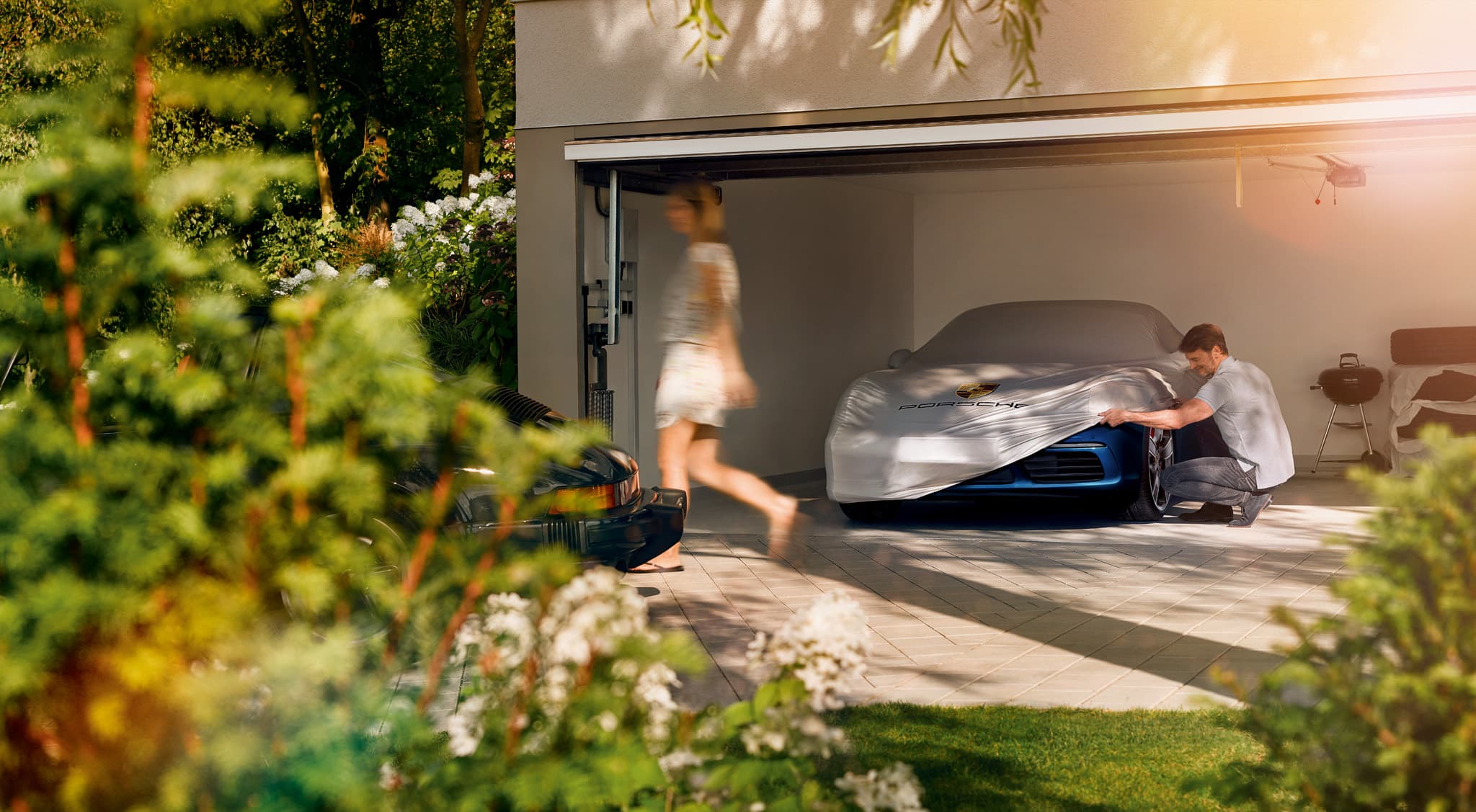 You can see a man in a garage next to a Porsche car beneath a car cover