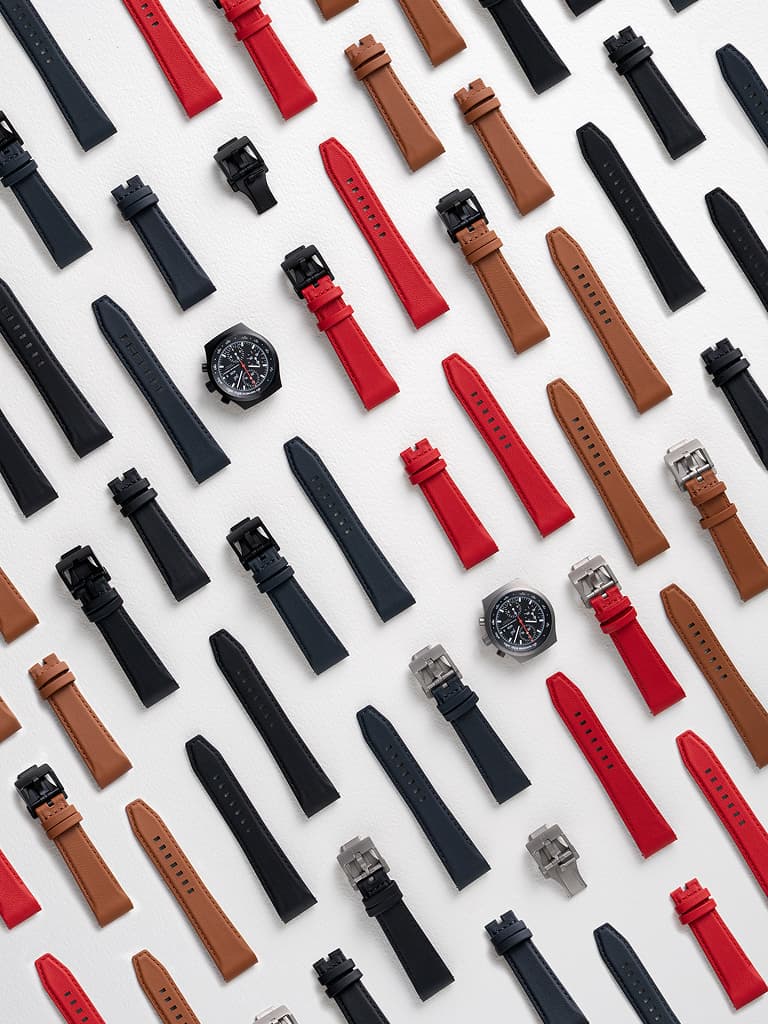 Gesorteerde horlogebandjes in zwart, rood en bruin op een witte achtergrond, met twee chronograafhorloges.