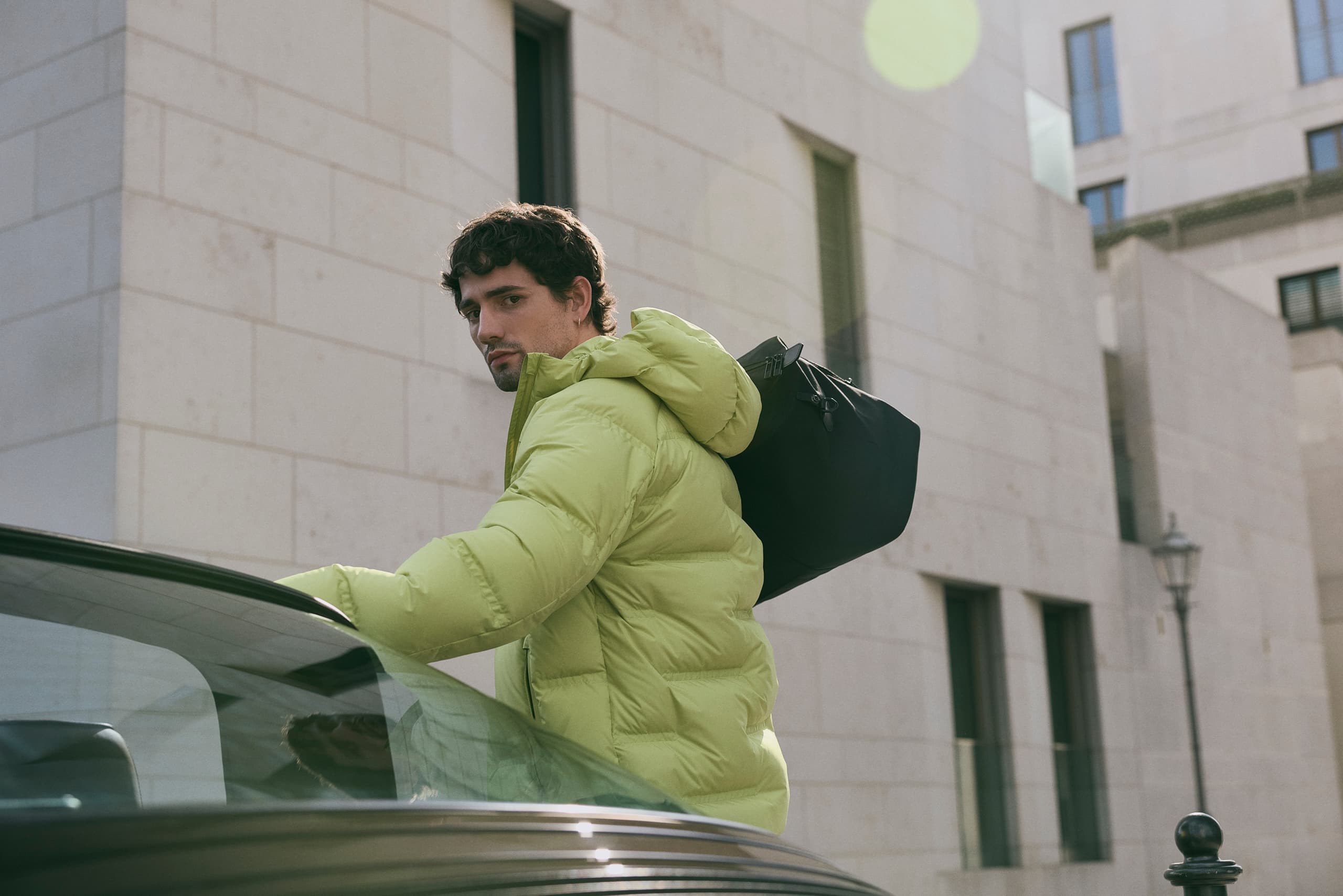 Man wearing Porsche Design jacket and bag in urban szenario, Porsche Car next to him