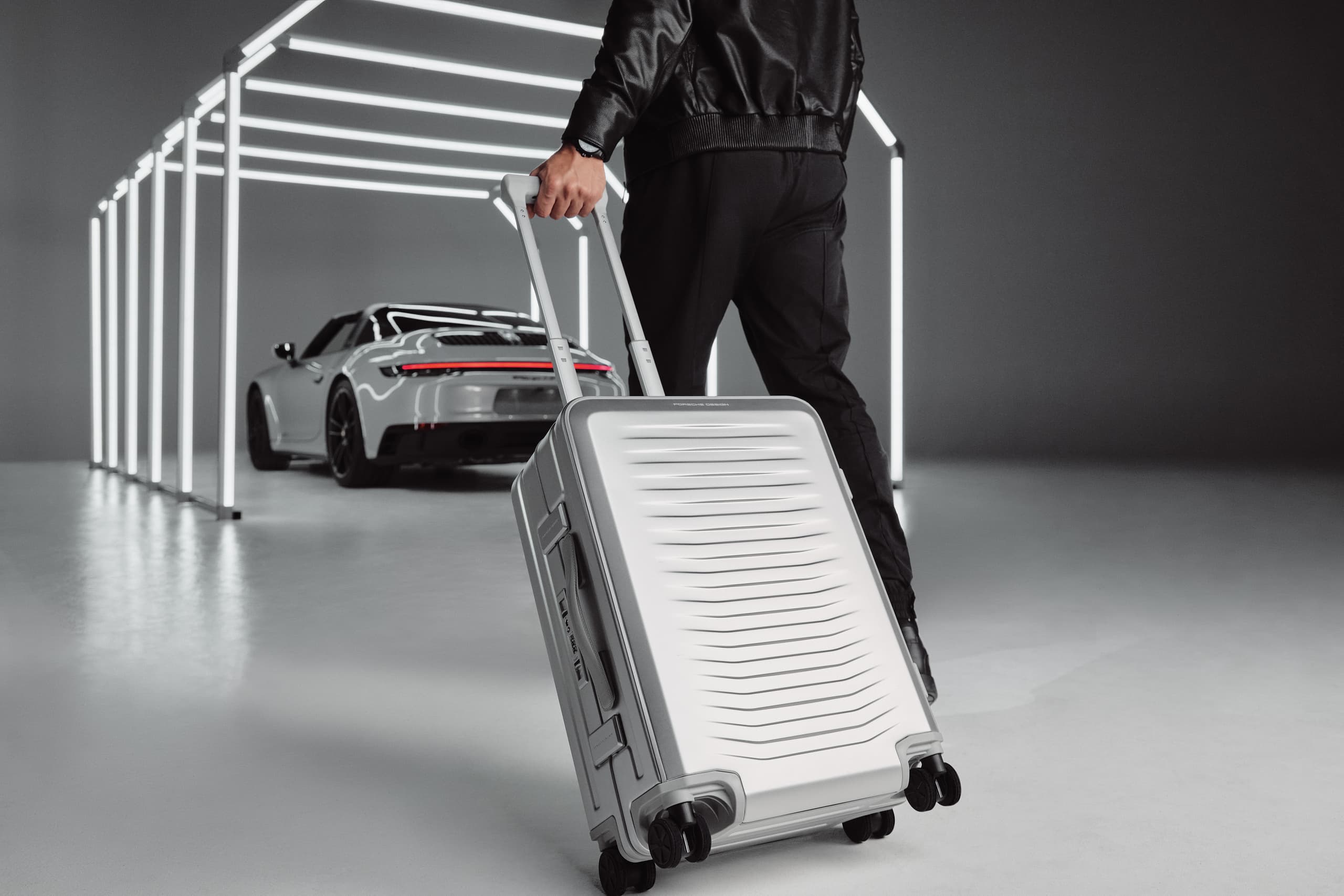 Person with a silver Porsche Design Aluminum trolley on the way to a silver Porsche 911