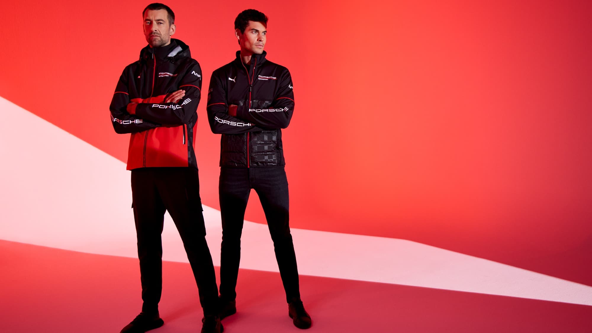 Two men in Porsche jackets stand confidently against a red background, showcasing sporty apparel.